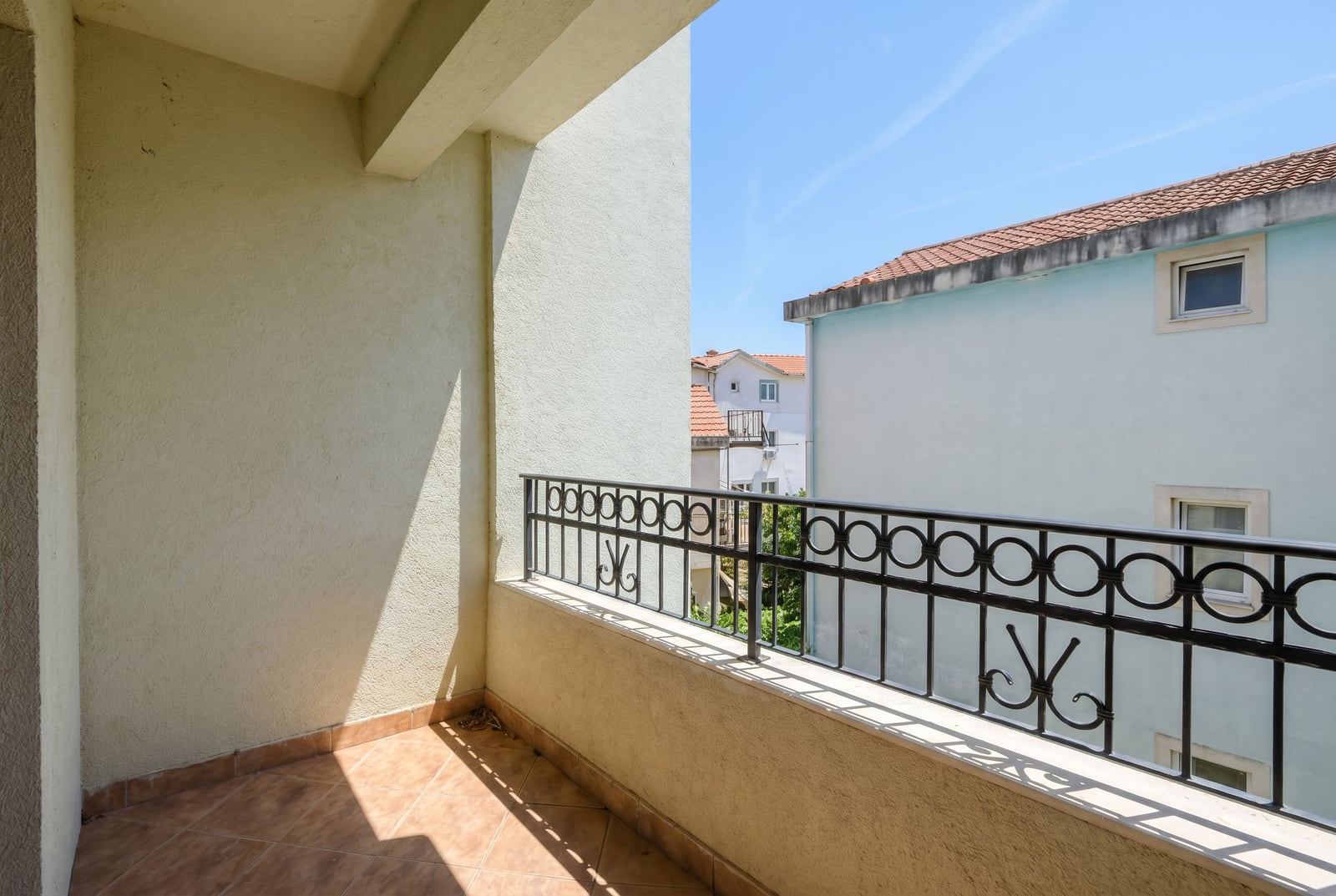 Open balcony with wrought iron railing and tiled floor in an apartment in Budva, Montenegro, overlooking neighboring buildings.