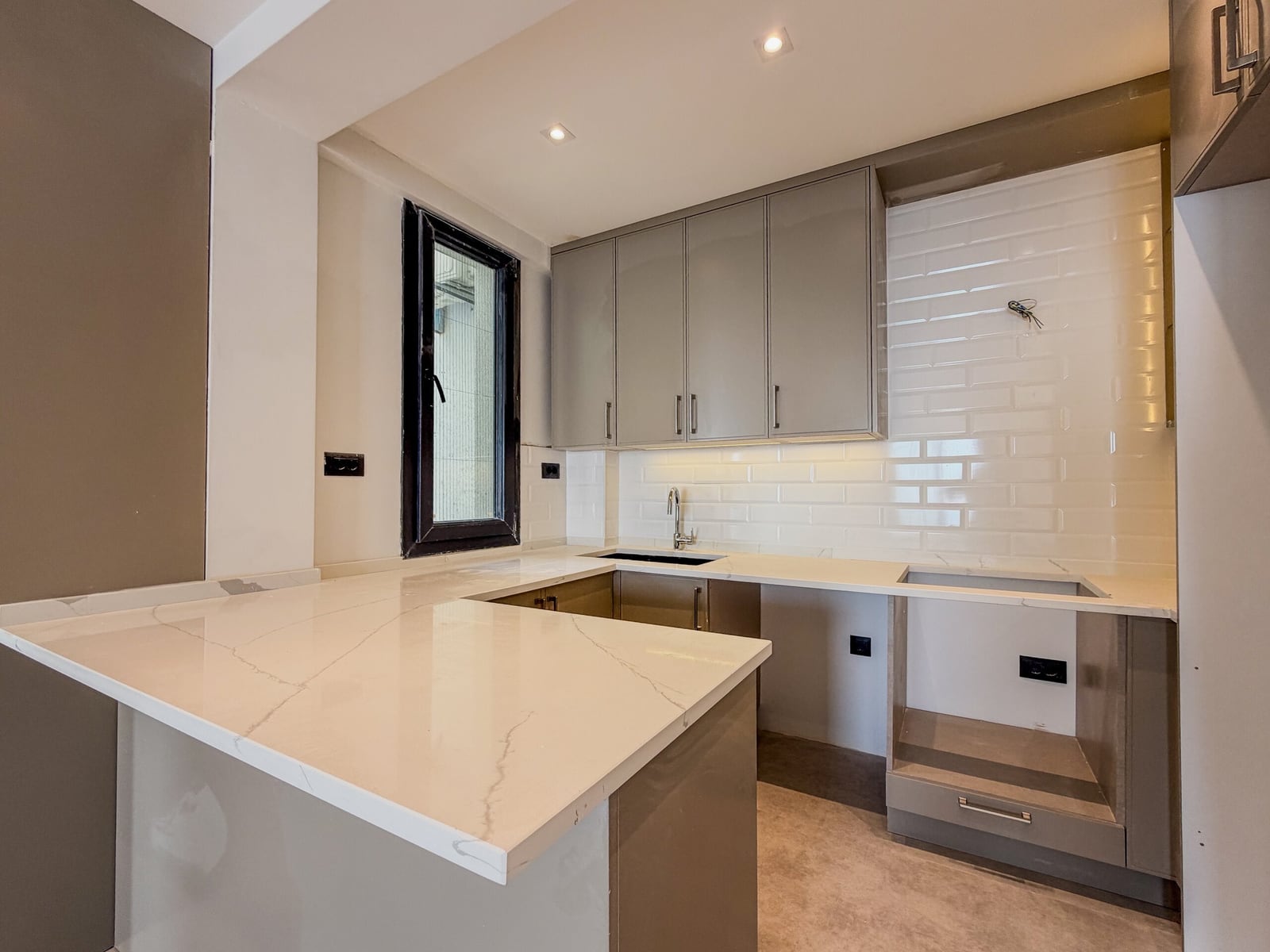 Modern kitchen featuring grey cabinets, a white marble island, and a white subway tile backsplash.