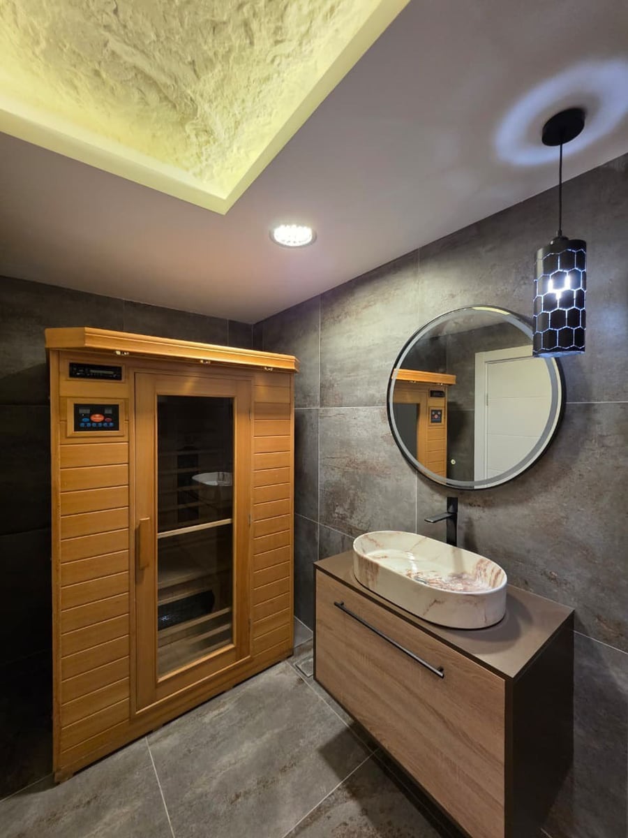 Bathroom with sauna in an apartment in Bečići, Montenegro: stylish finishes, a vessel sink, and a round mirror.