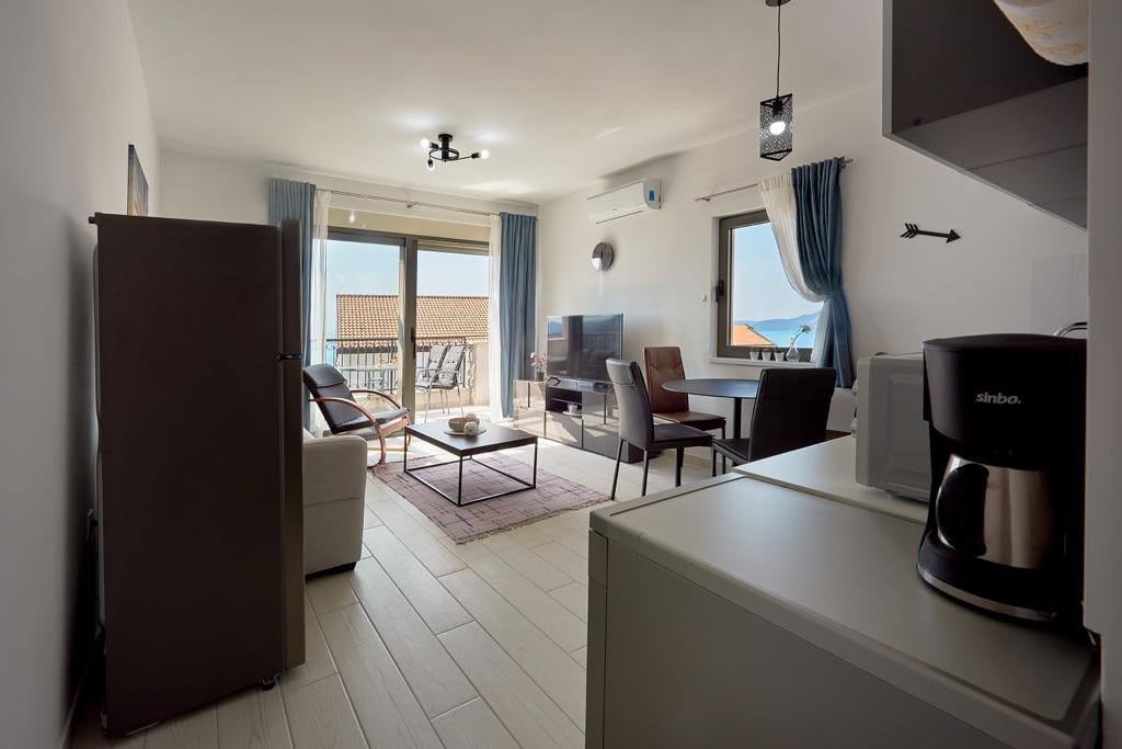 Living room with kitchen in an apartment in Pržno, Montenegro: modern furniture, bright interior, and a sea view from the balcony.