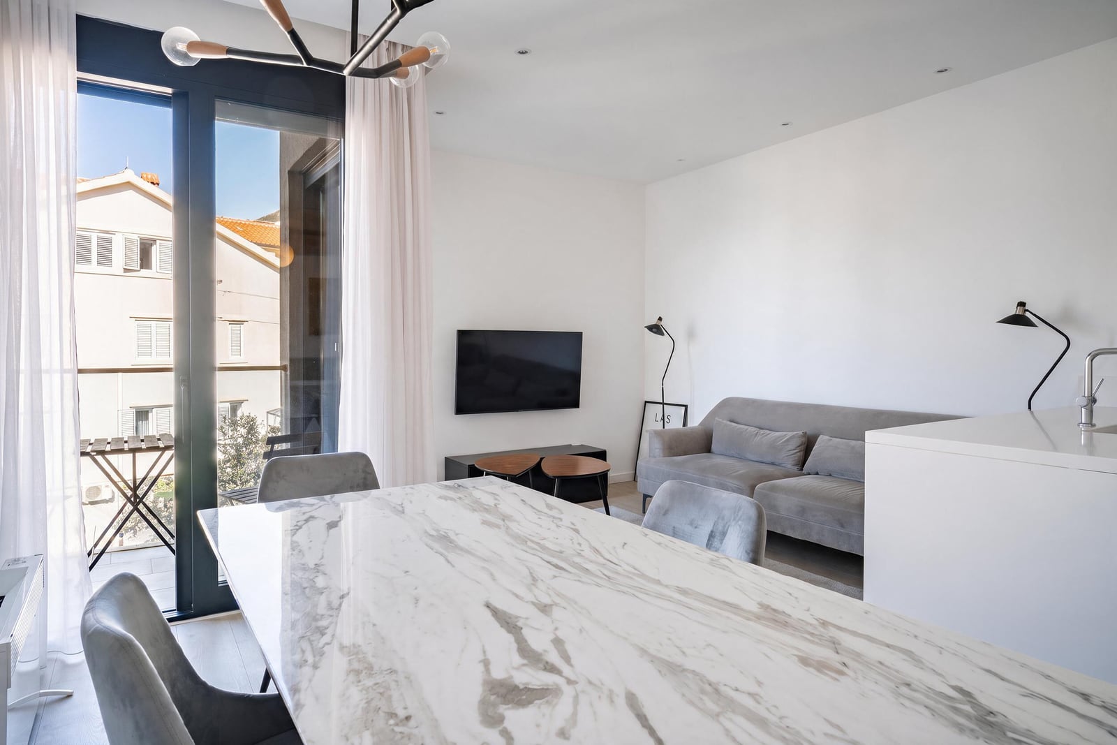 Living room with a marble table, gray sofa, and panoramic window in an apartment in Tivat, Montenegro