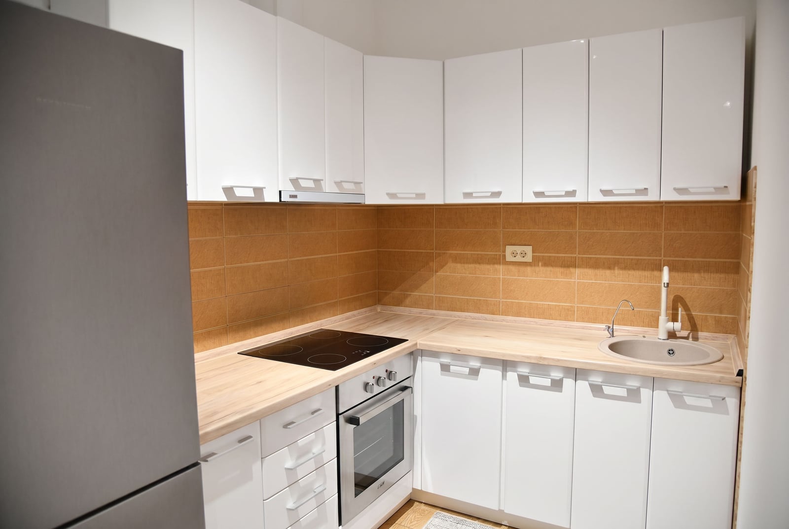 Modern white kitchen with appliances in an apartment for sale, Becici, Montenegro: built-in stove, sink, and backsplash.