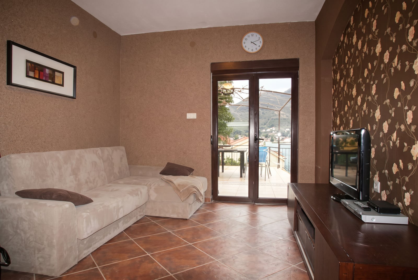Cozy living room with a beige sofa, TV area, and panoramic access to a terrace with a sea view in a house in Tivat, Montenegro.
