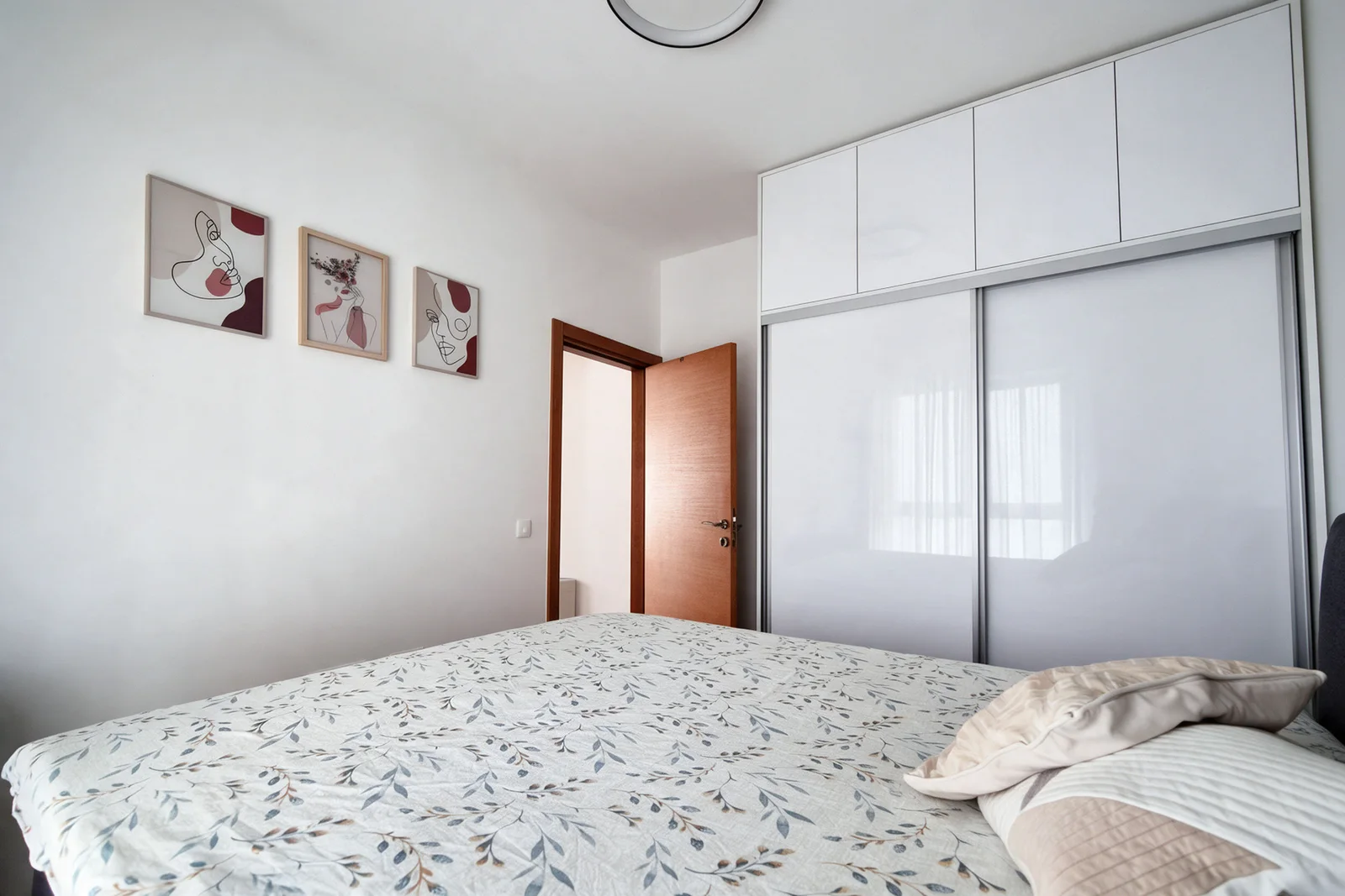 Bedroom featuring a bed with floral bedding, a white sliding wardrobe, and three framed art prints on the wall.
