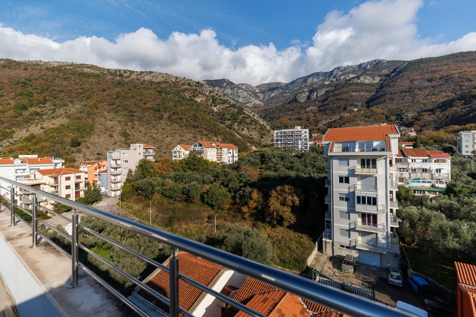 View from the penthouse balcony overlooking the mountains and a residential complex in Bečići, Montenegro: modern development and olive groves.
