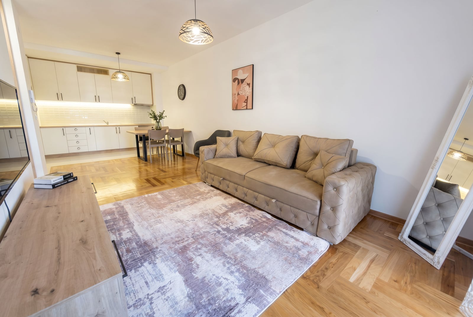 Living room with a beige sofa and kitchen in a modern apartment in Rafailovici, Montenegro. Parquet flooring and stylish interior.