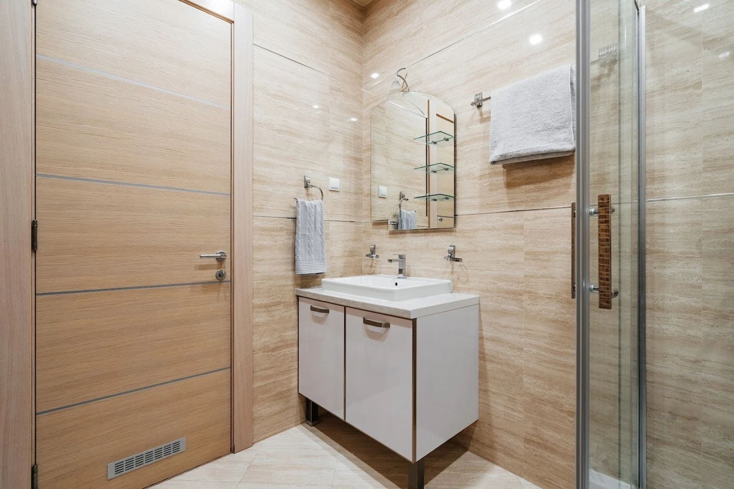 Modern bathroom in an apartment in Budva, Montenegro: white vanity with sink, shower cabin, and beige tiles.