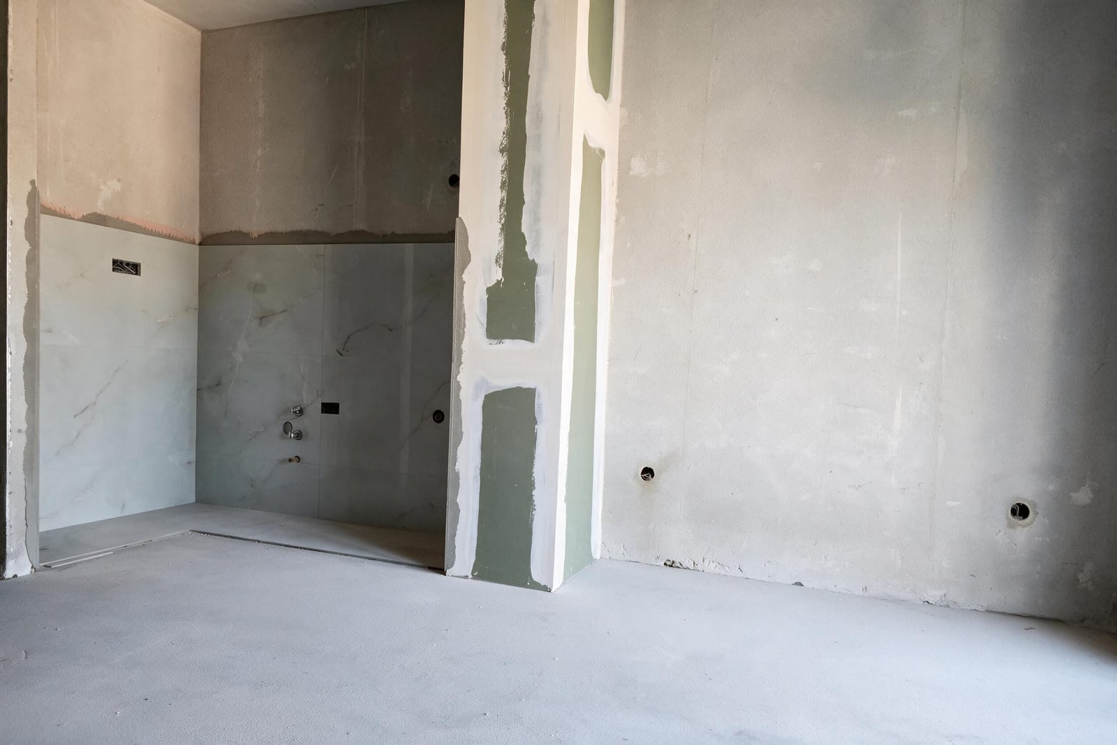 Unfinished bathroom featuring installed marble tiles and exposed shower faucet fixtures.