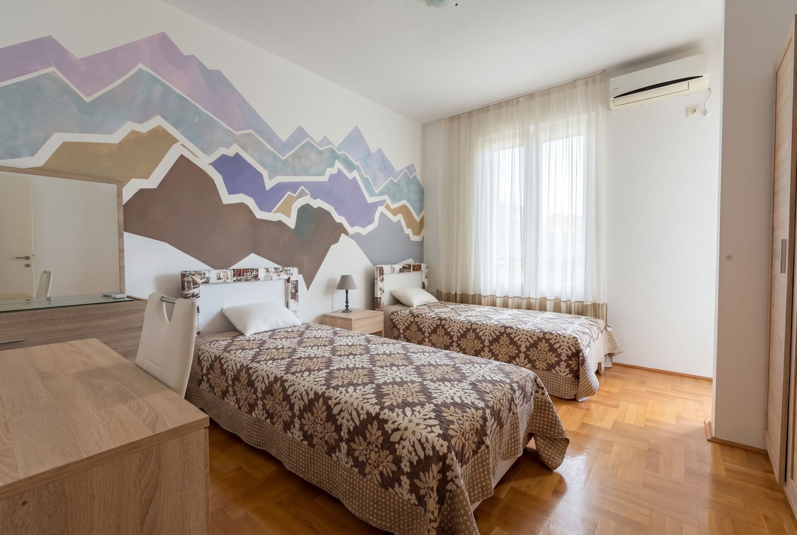 Bedroom with two beds and a mountain mural on the wall in an apartment in Bečići, Budva, Montenegro. Bright interior with parquet flooring.