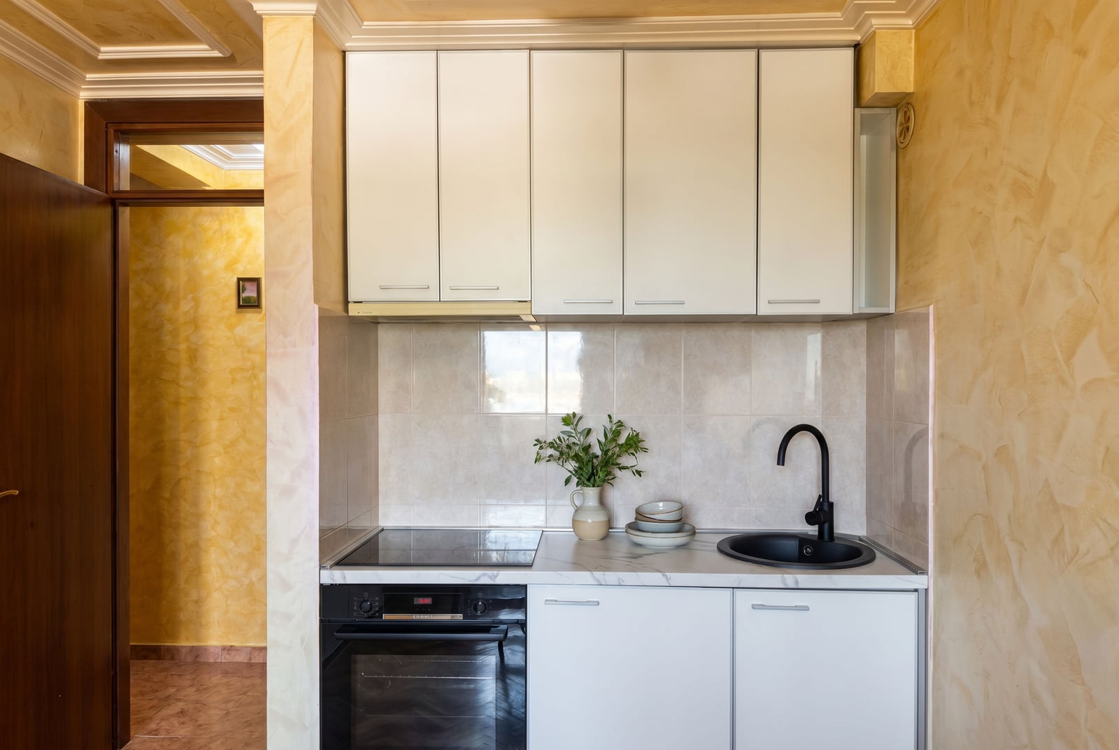 Compact white kitchen with black fixtures in an apartment for sale in Budva, Montenegro. Built-in appliances and decor.