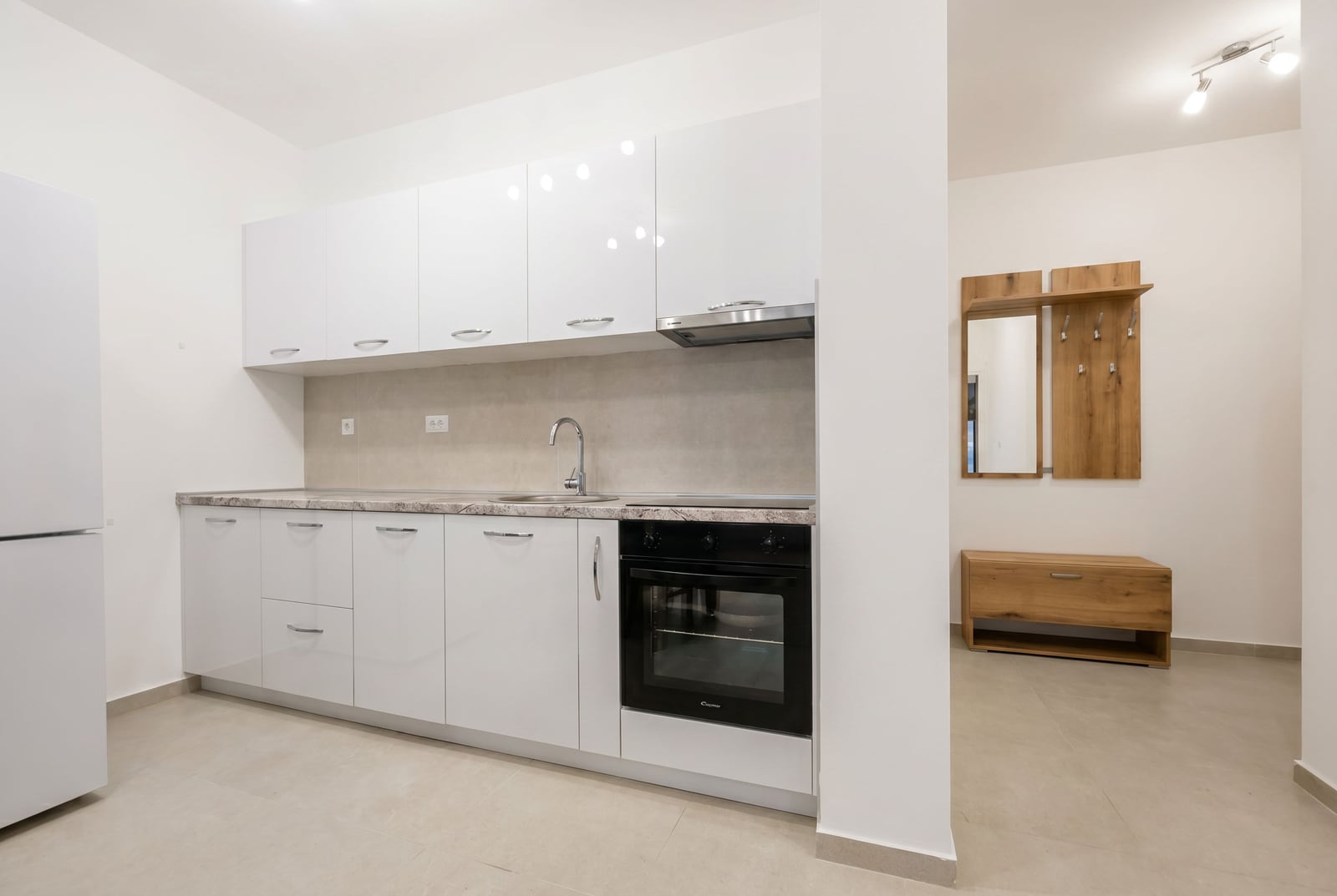 Modern white kitchen and hallway in an apartment in Bečići, Montenegro: built-in appliances and light wood furniture.