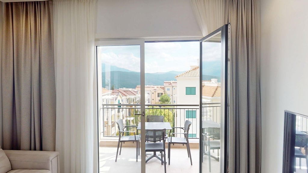 View from the balcony of an apartment in Luštica, Montenegro: a terrace with furniture and a panoramic view of the mountains and the Lustica Bay residential complex.