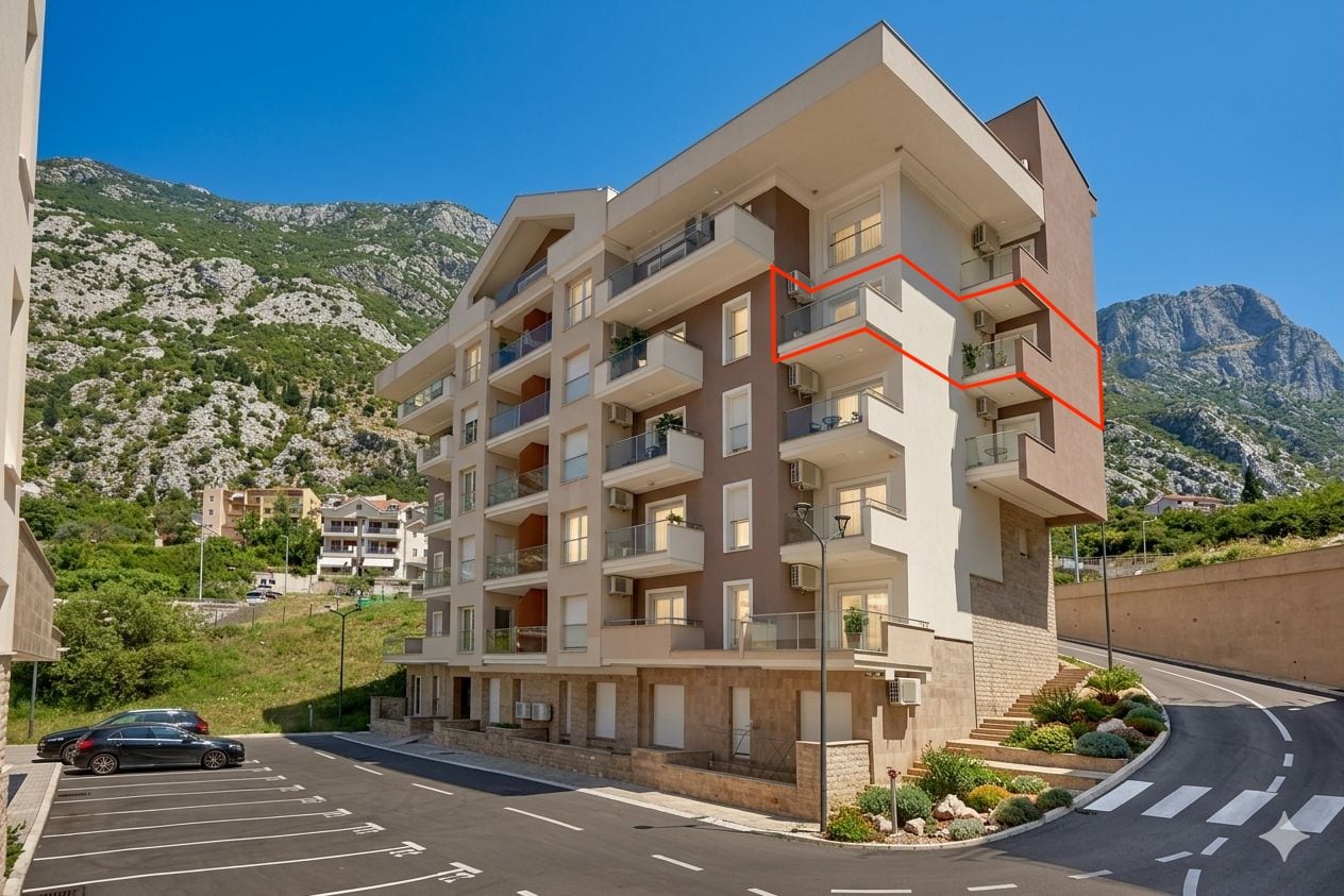 Modern residential complex with balconies in Dobrota, Montenegro: view of the building with parking and mountain landscape.