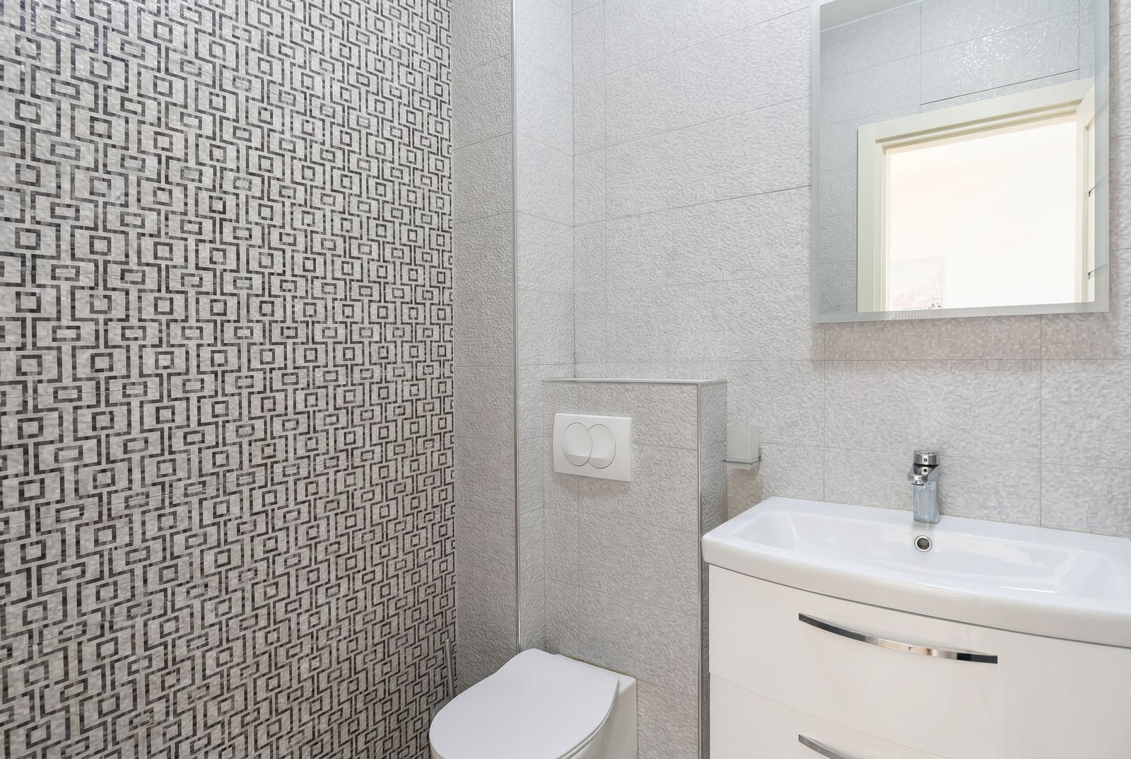 Modern bathroom in an apartment in Bečići, Montenegro: white furniture, wall-hung toilet, and patterned tiles.