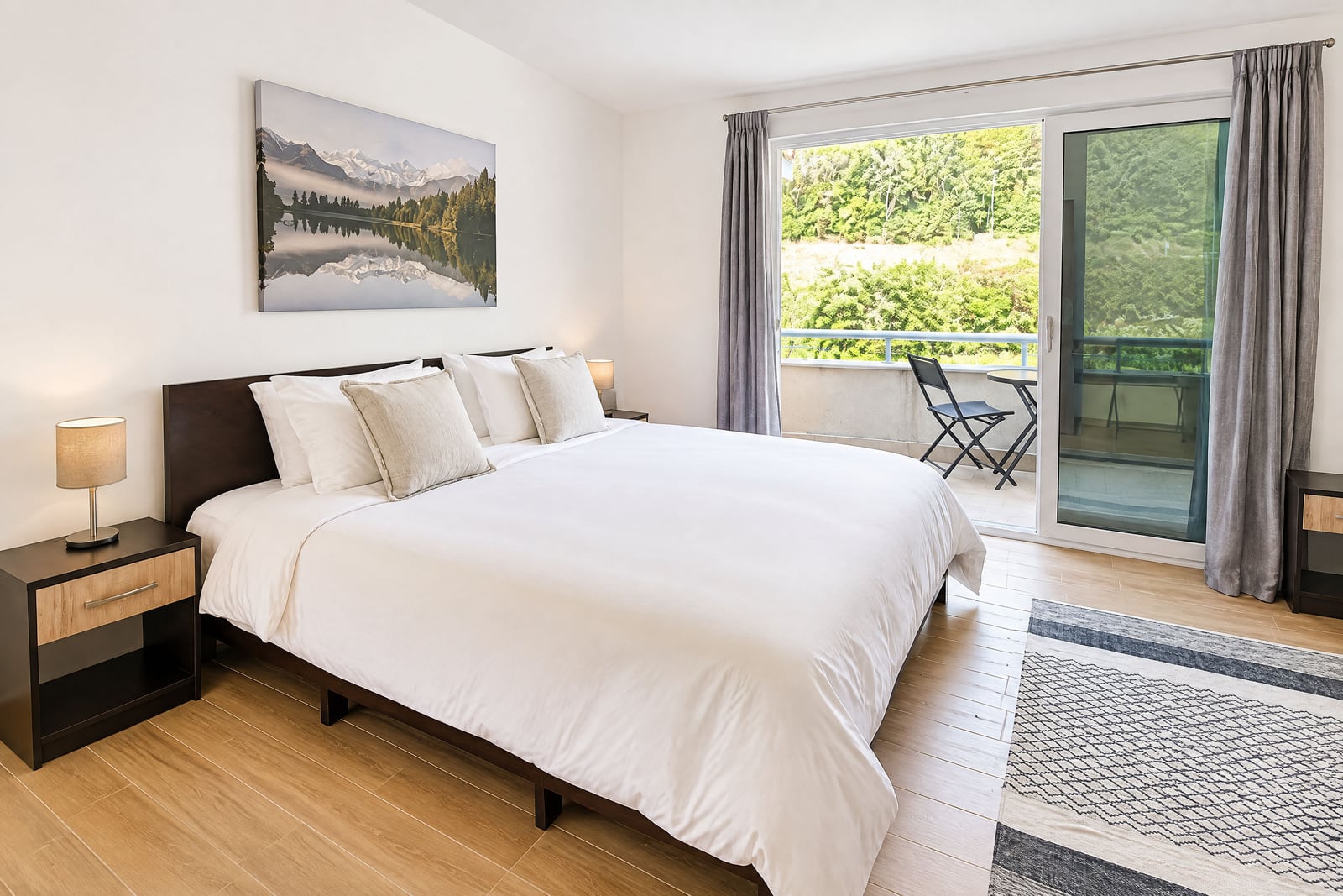 Modern bedroom featuring a large bed with white linens, nightstands, and a sliding door leading to a balcony.