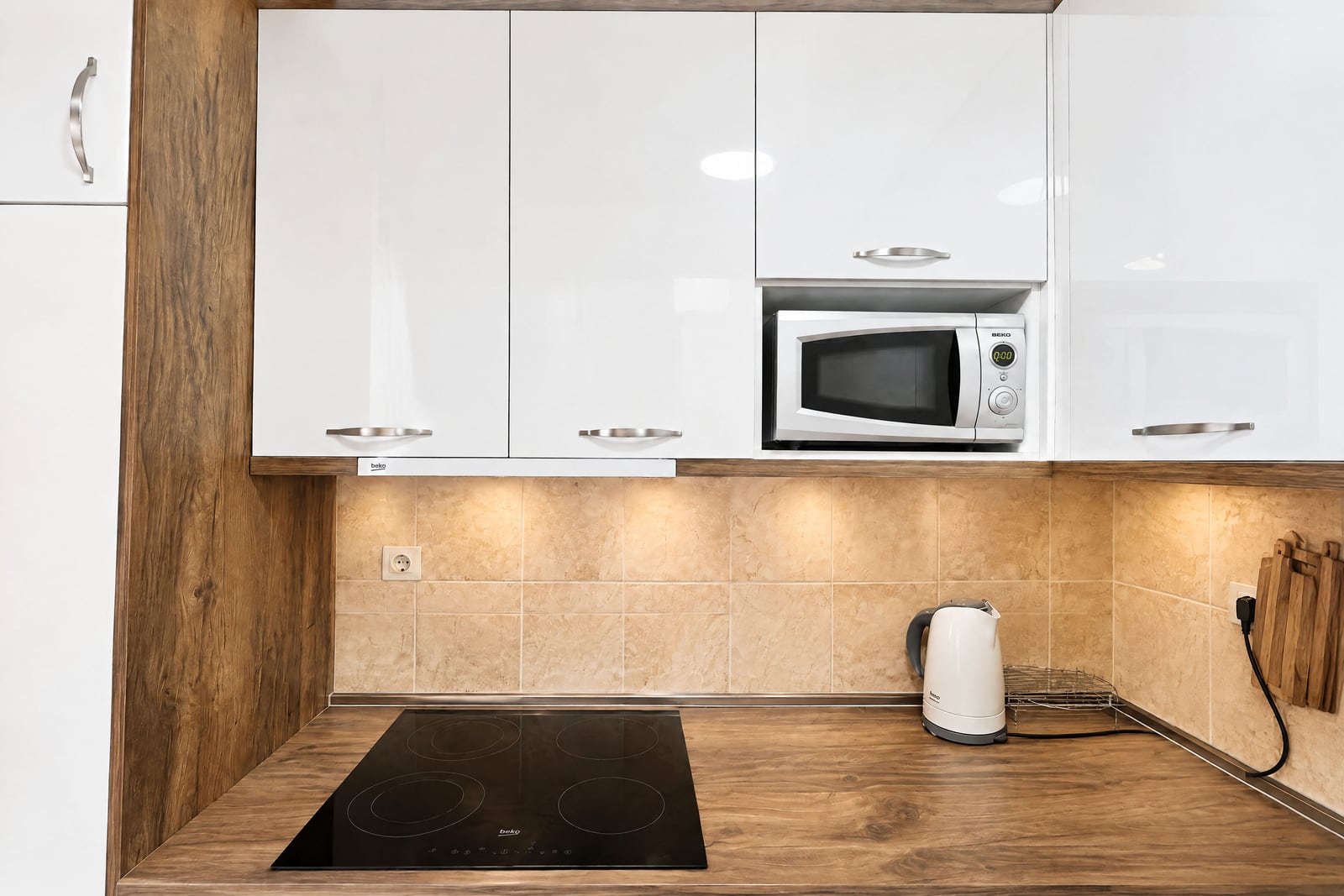 Kitchen with glossy white cabinets, wood countertop, black induction cooktop, microwave, and electric kettle.
