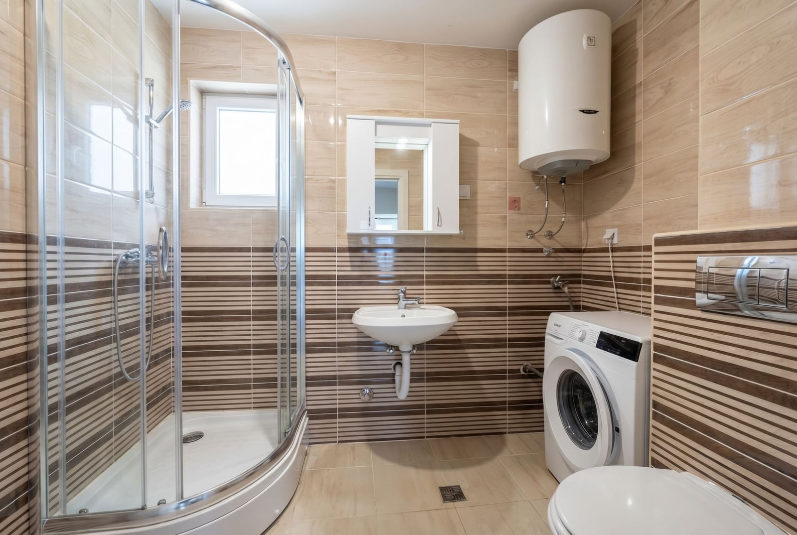 Bathroom in an apartment in Budva, Montenegro: shower cabin, washing machine, water heater, and tiled finish.