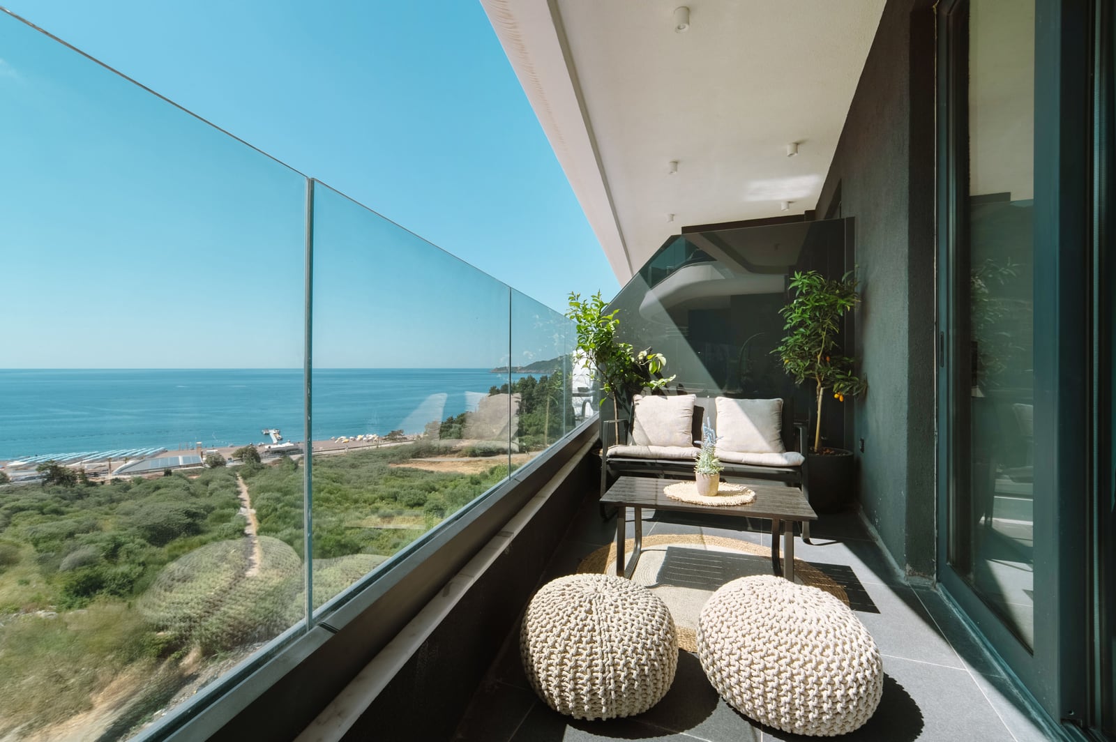 Terrace with panoramic sea view in the Bečići residential complex, Montenegro: wicker furniture, glass railing, and beach view.