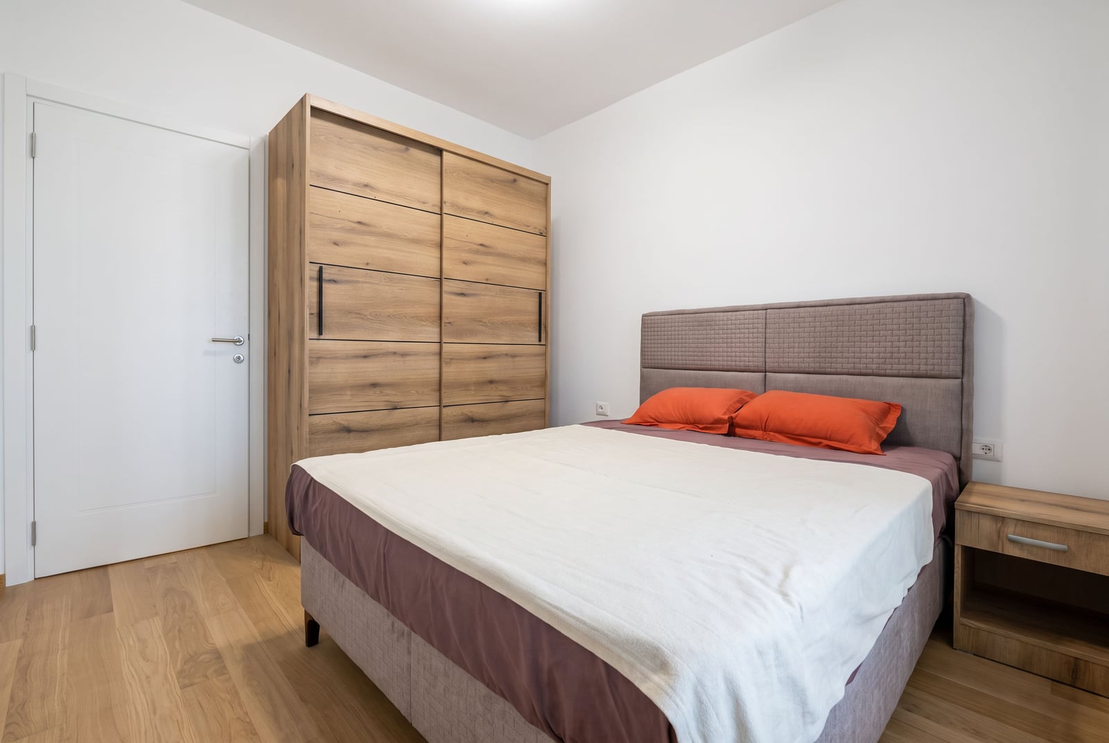 Modern bedroom featuring a double bed with orange pillows, a large wooden sliding wardrobe, and a nightstand.