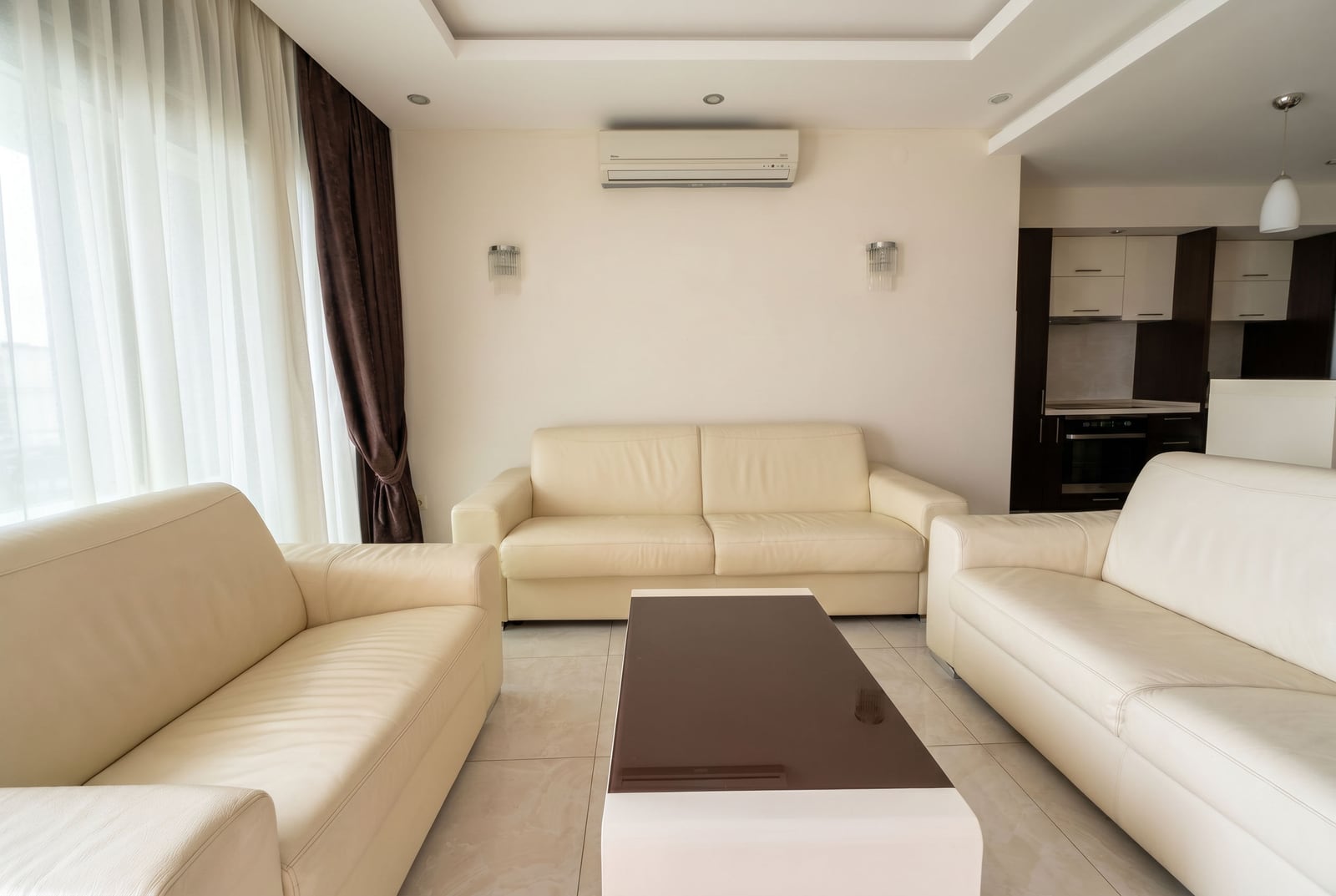 Living room with white leather sofas and a kitchen in an apartment in Bečići, Montenegro. Modern interior with air conditioning.