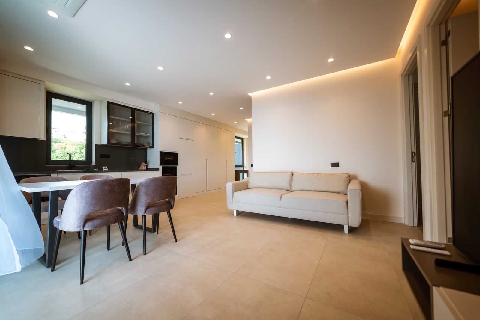 Modern living room with kitchen in an apartment in Bečići, Montenegro: light-colored sofa, dining area, and built-in furniture.