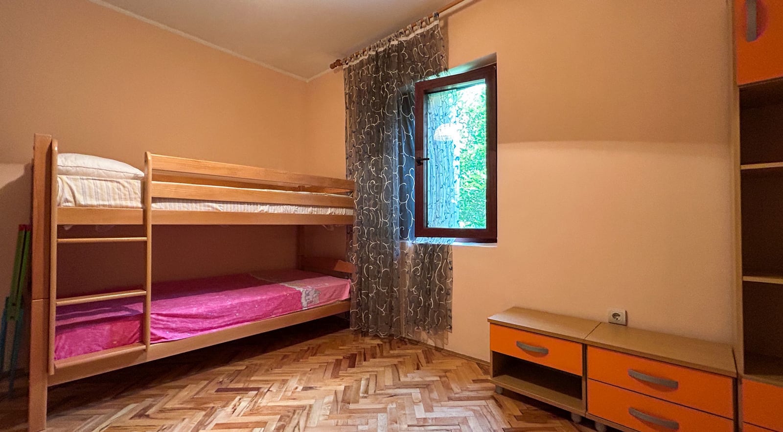 Children’s bedroom with a bunk bed in a villa, Dobrota, Montenegro: parquet floor, orange furniture, and a garden view.