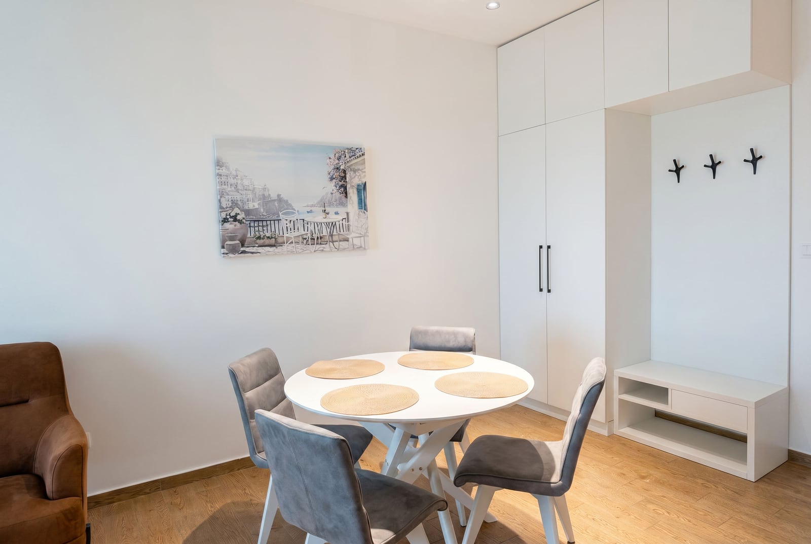 Modern living room with a dining area in an apartment, Bečići, Montenegro: white table, grey chairs, and built-in wardrobe.