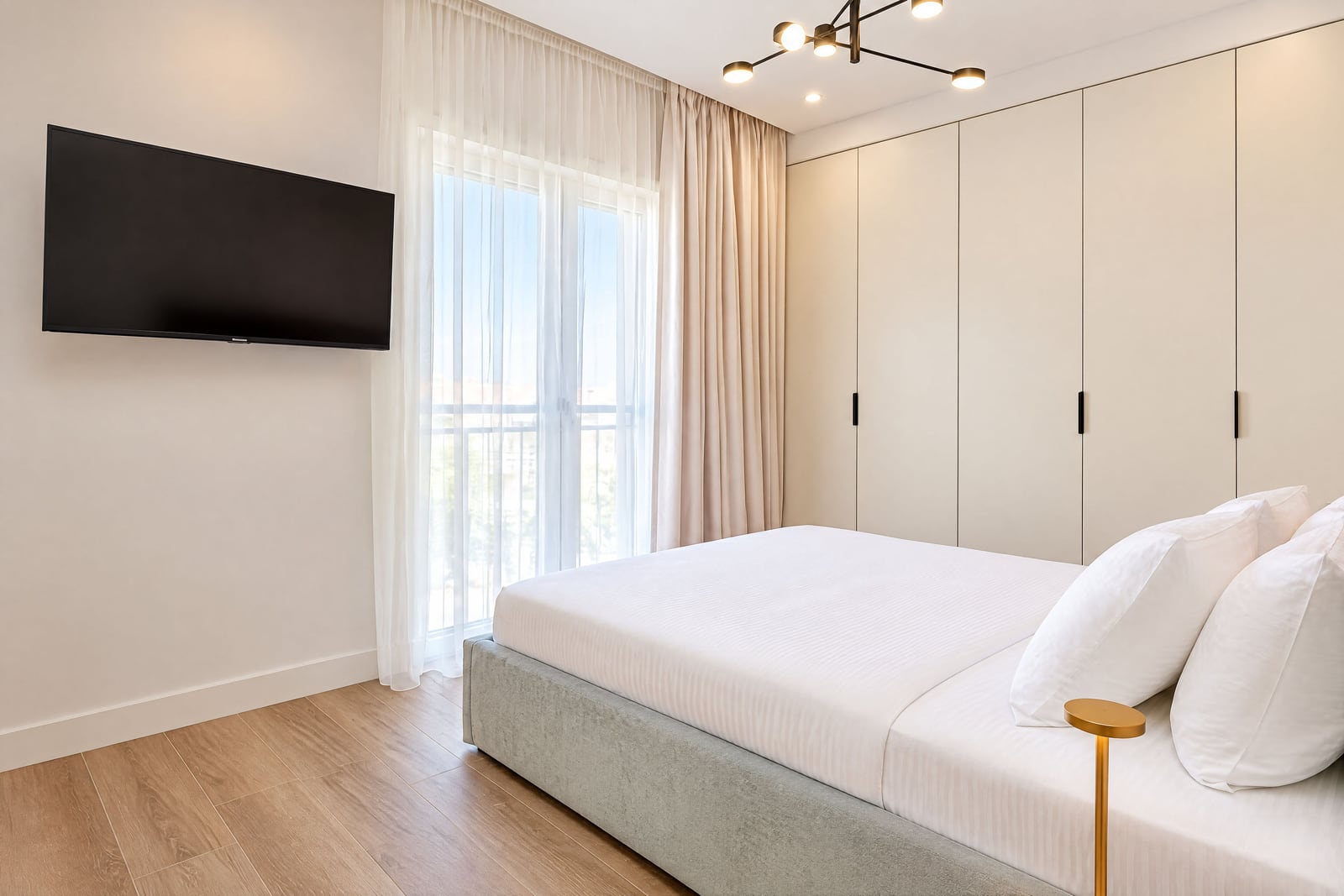 Modern bedroom featuring a white bed, built-in wardrobe, and wall-mounted TV near a window.