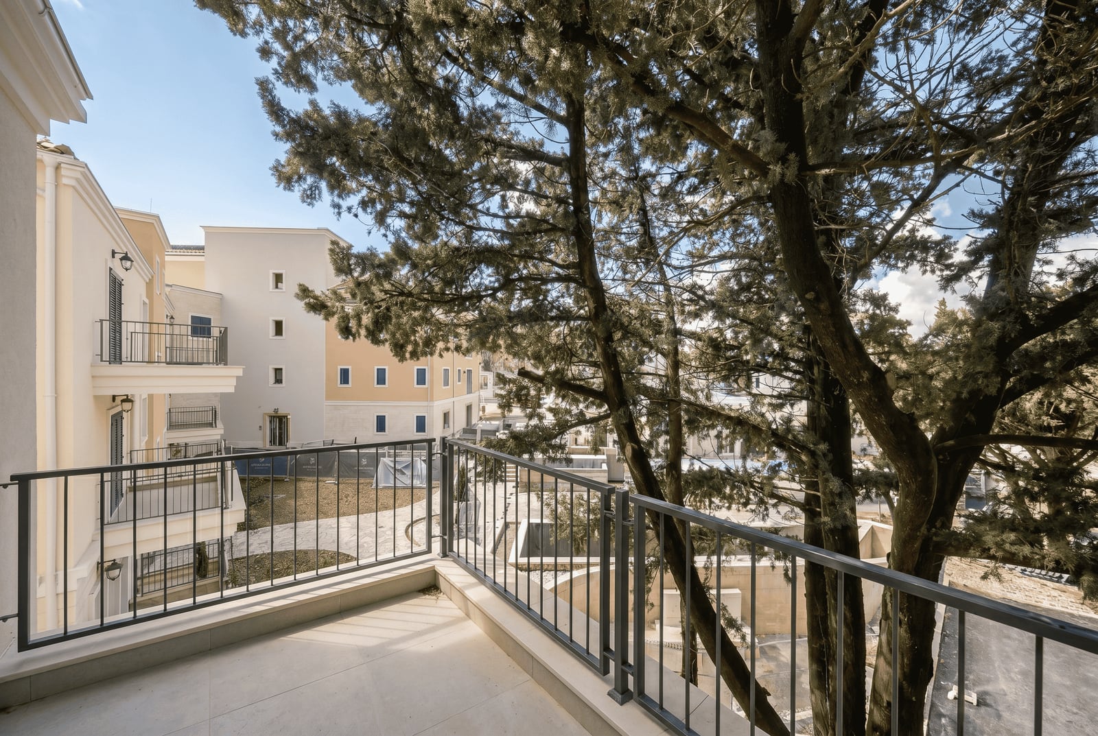 View from the balcony of a modern apartment in the Luštica residential complex, Montenegro: light facade finishes and pine trees nearby.