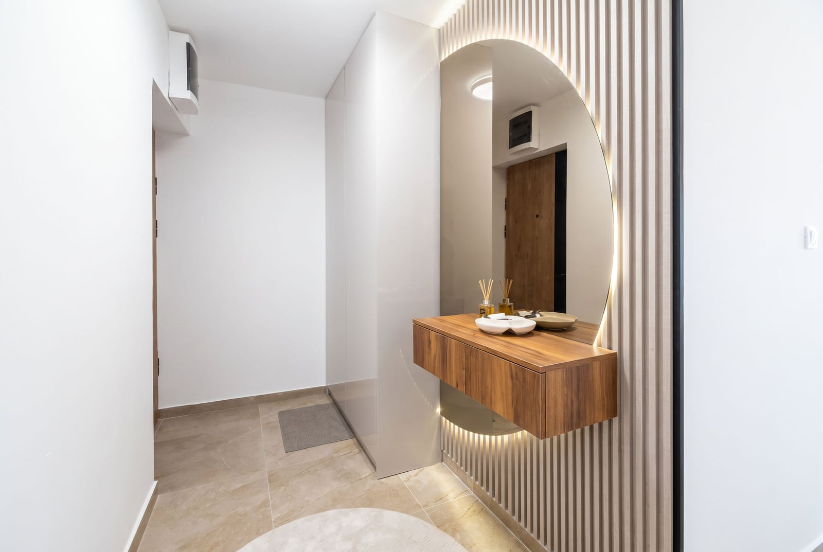 Modern bathroom with a floating wooden vanity, round backlit mirror, and slatted wall paneling.