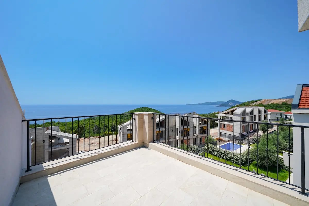 Open terrace of a villa in Reževići, Montenegro, with a panoramic view of the sea, mountains, and a residential complex under construction.