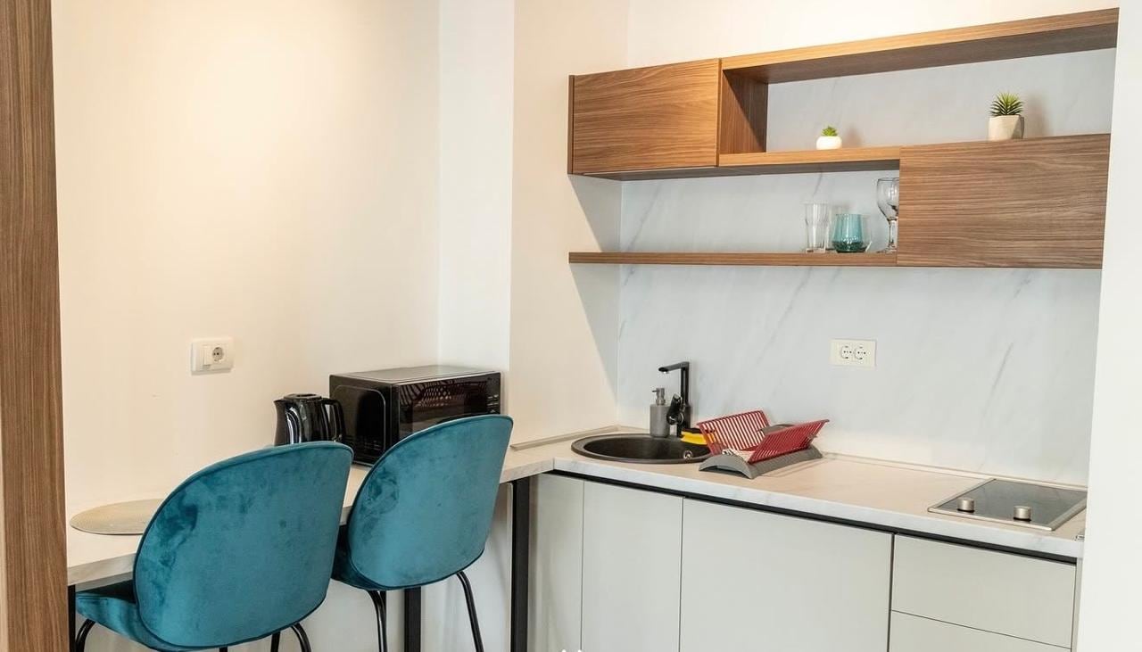 Modern kitchen in an apartment in Bečići, Montenegro: light-colored cabinetry, breakfast bar, and blue velvet chairs.
