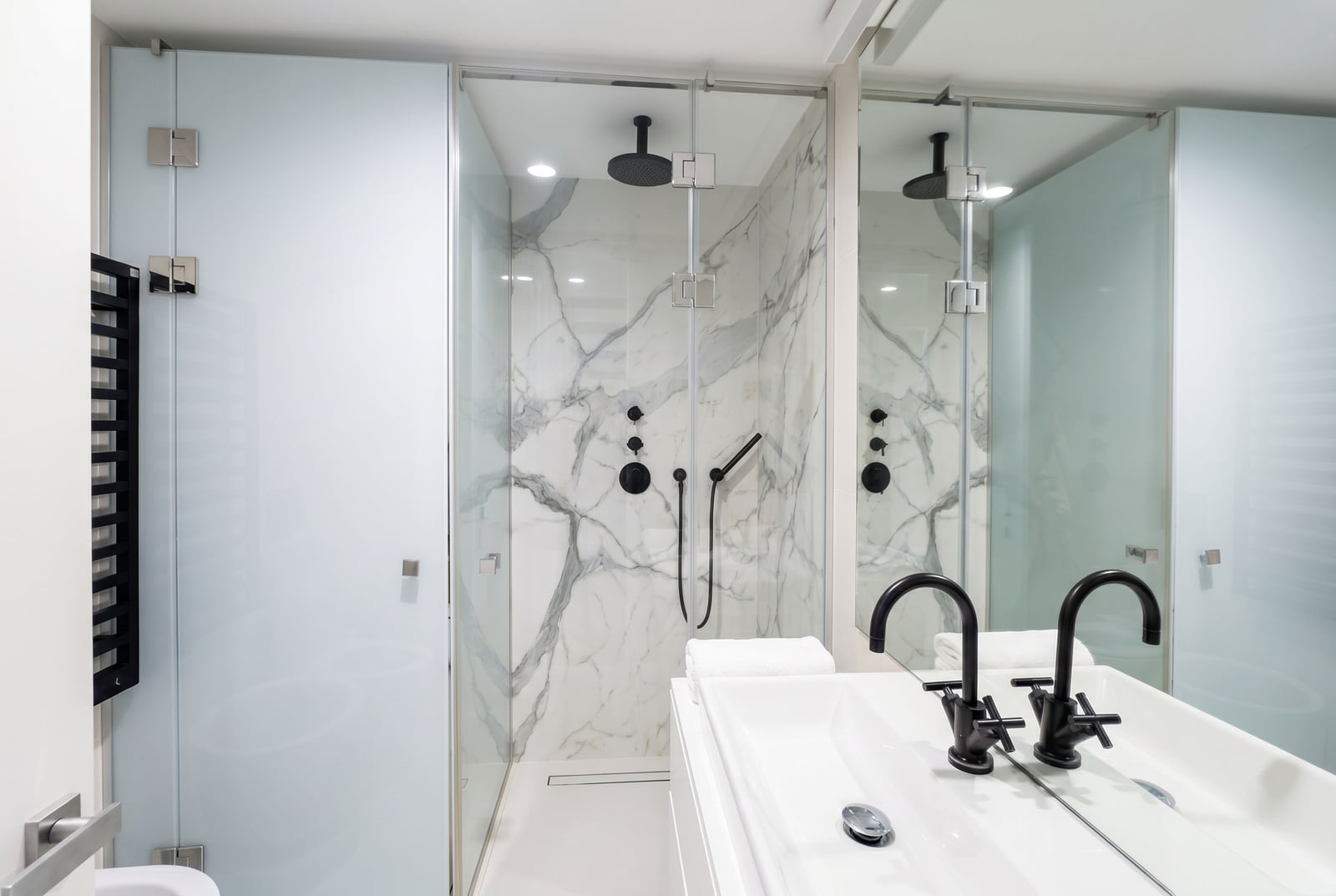 Modern bathroom in a Budva apartment, Montenegro: shower cabin with marble-effect finish and black fixtures.