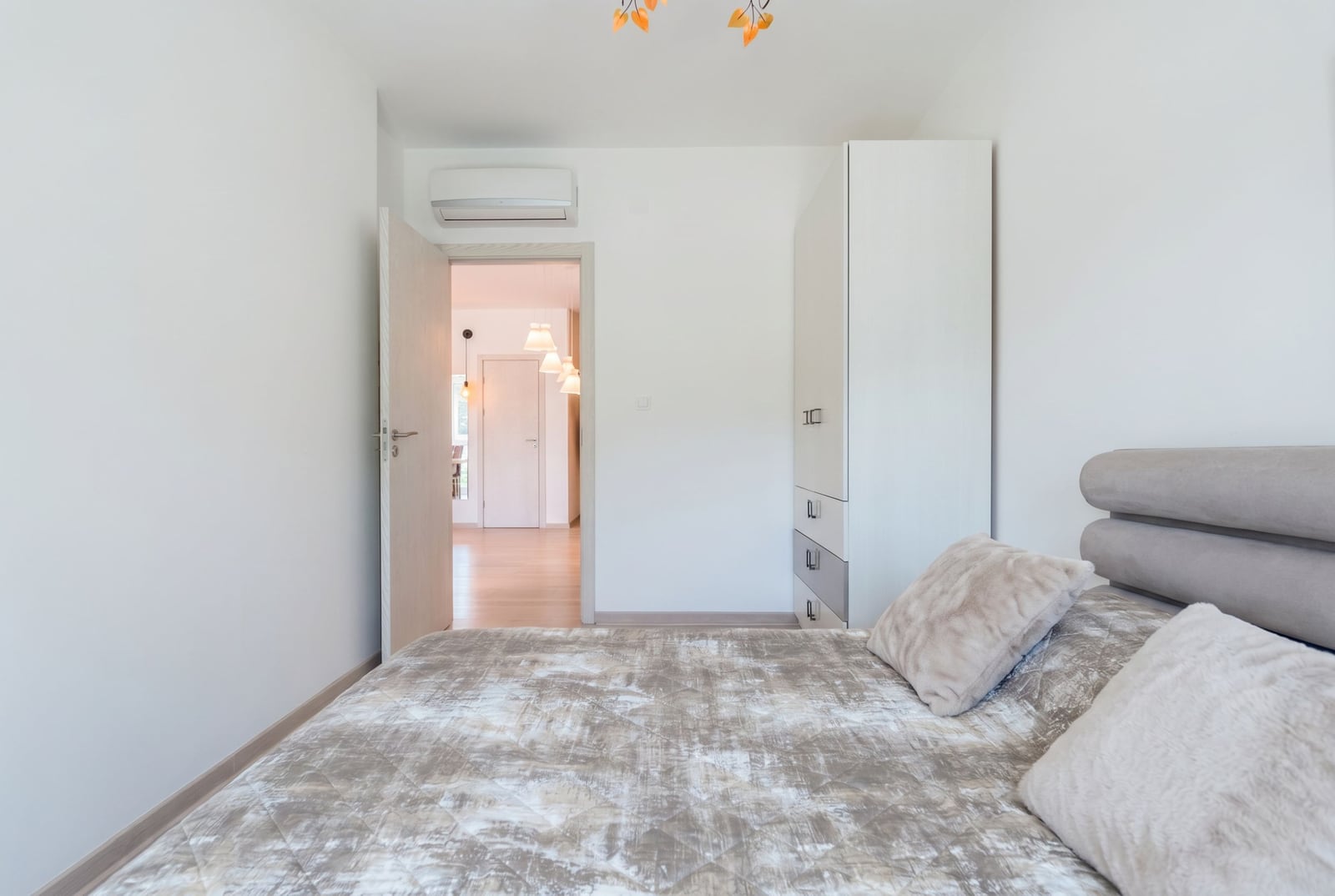 Bright bedroom in an apartment in Bečići, Montenegro: double bed, white wardrobe, air conditioner, and view of the hallway.