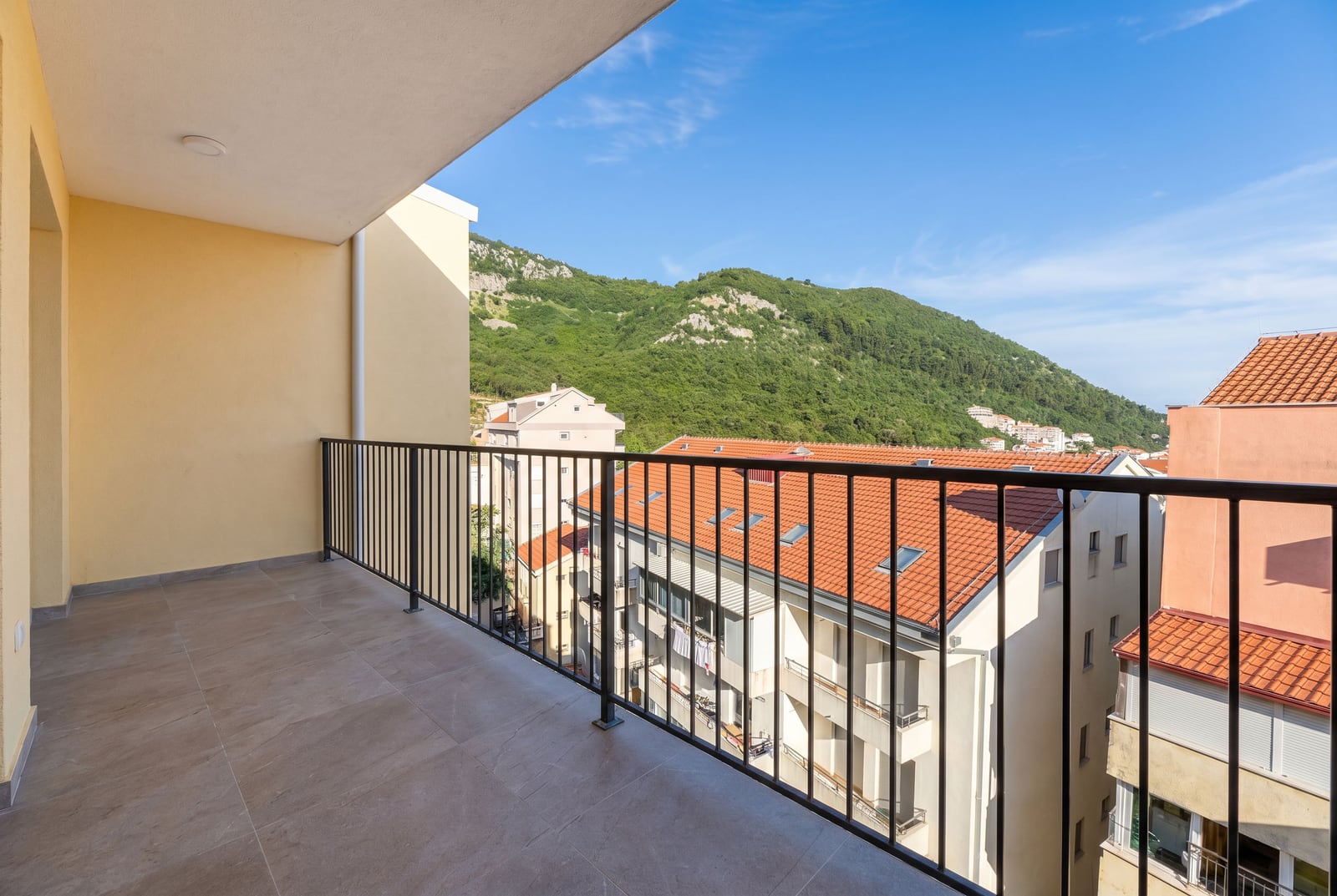 Spacious balcony with mountain and city views in an apartment, Budva, Montenegro, tiled floor and metal railing.