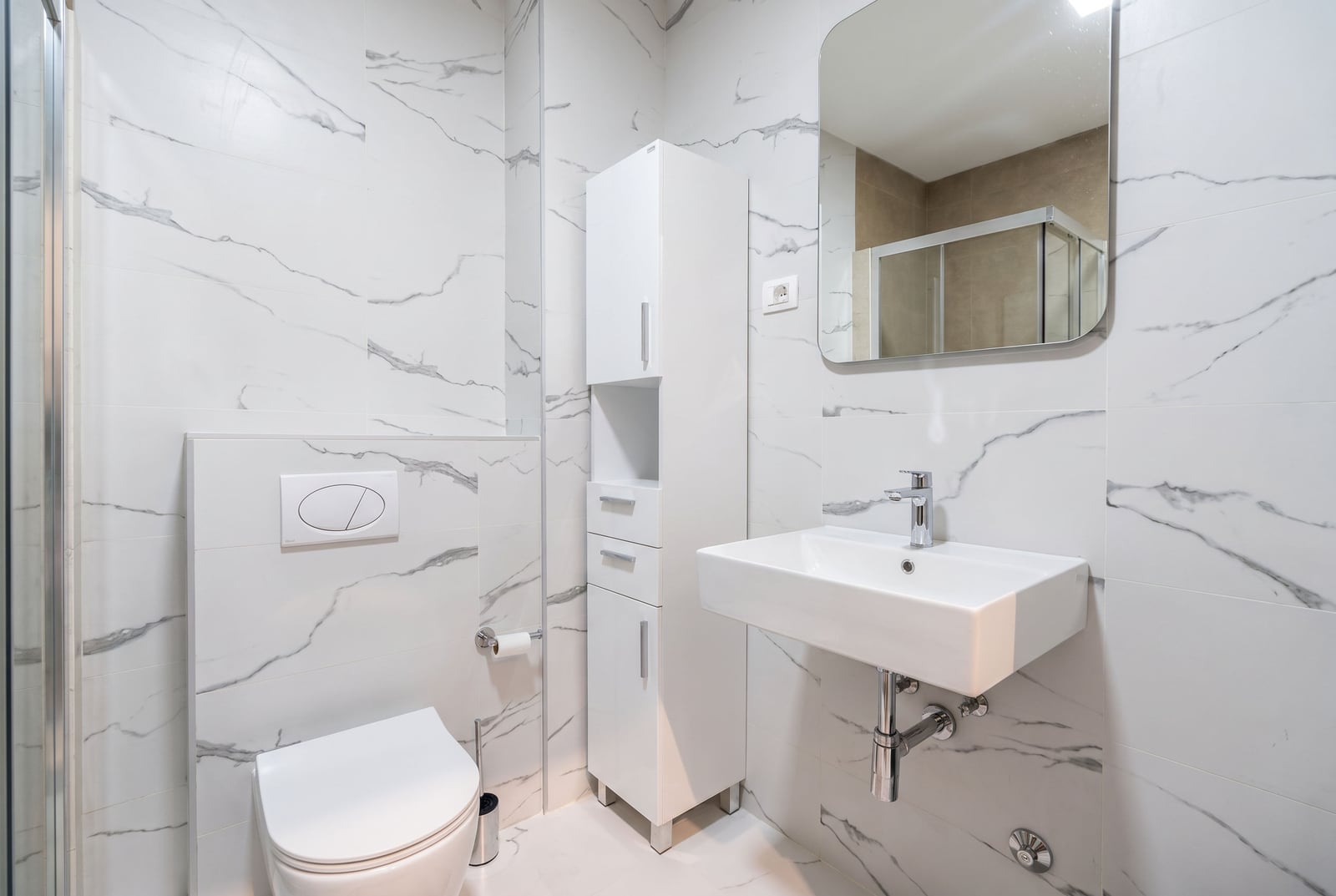 Modern bathroom with white marble tile, sink, wall-hung toilet, and cabinet in an apartment in Budva, Montenegro.