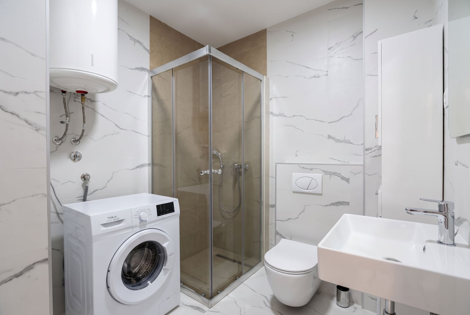 Modern bathroom with a shower cabin, washing machine, and water heater in an apartment in Budva, Montenegro