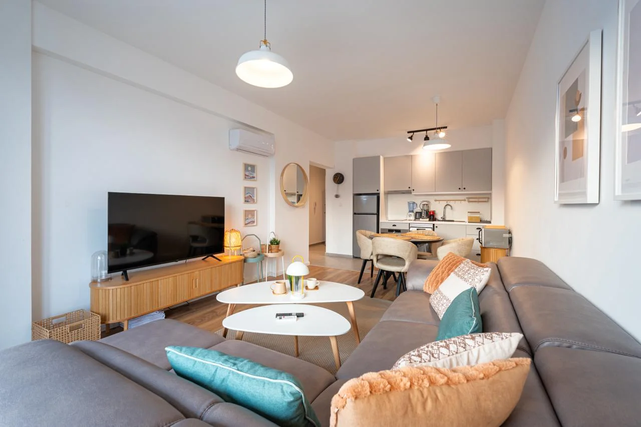 Modern living room with a grey sofa, TV, and visible kitchen area in the background.