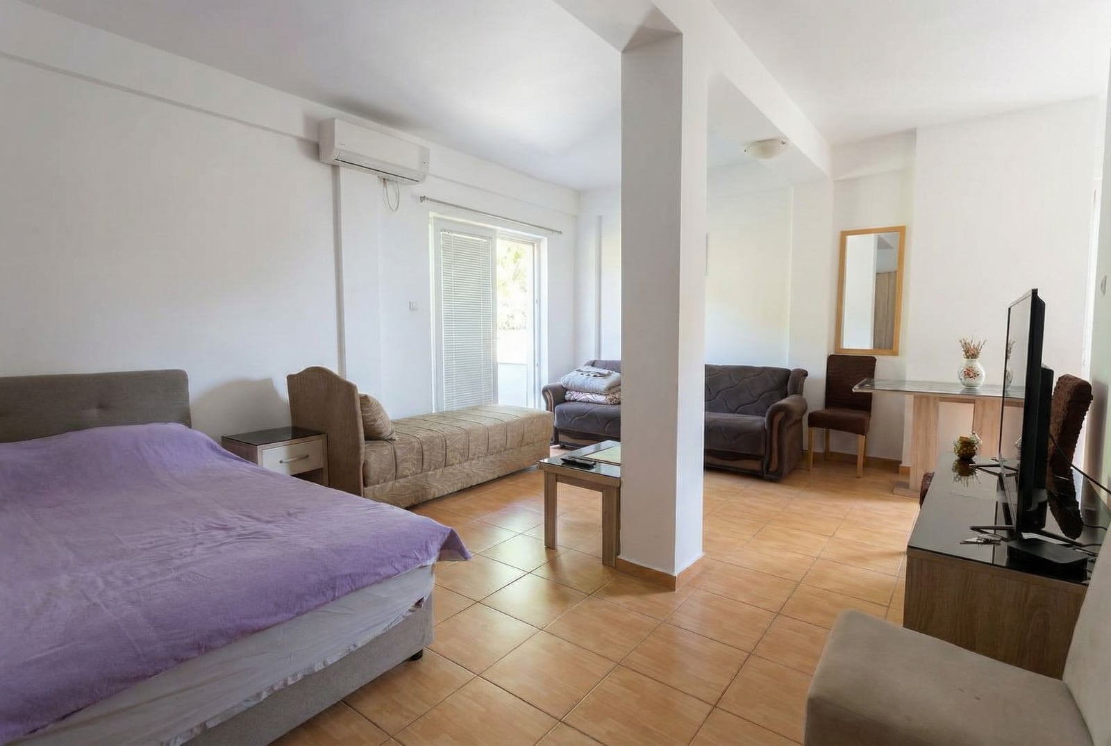 Bright studio in Budva, Montenegro: living room with a double bed, sofa, TV area, and access to the balcony.