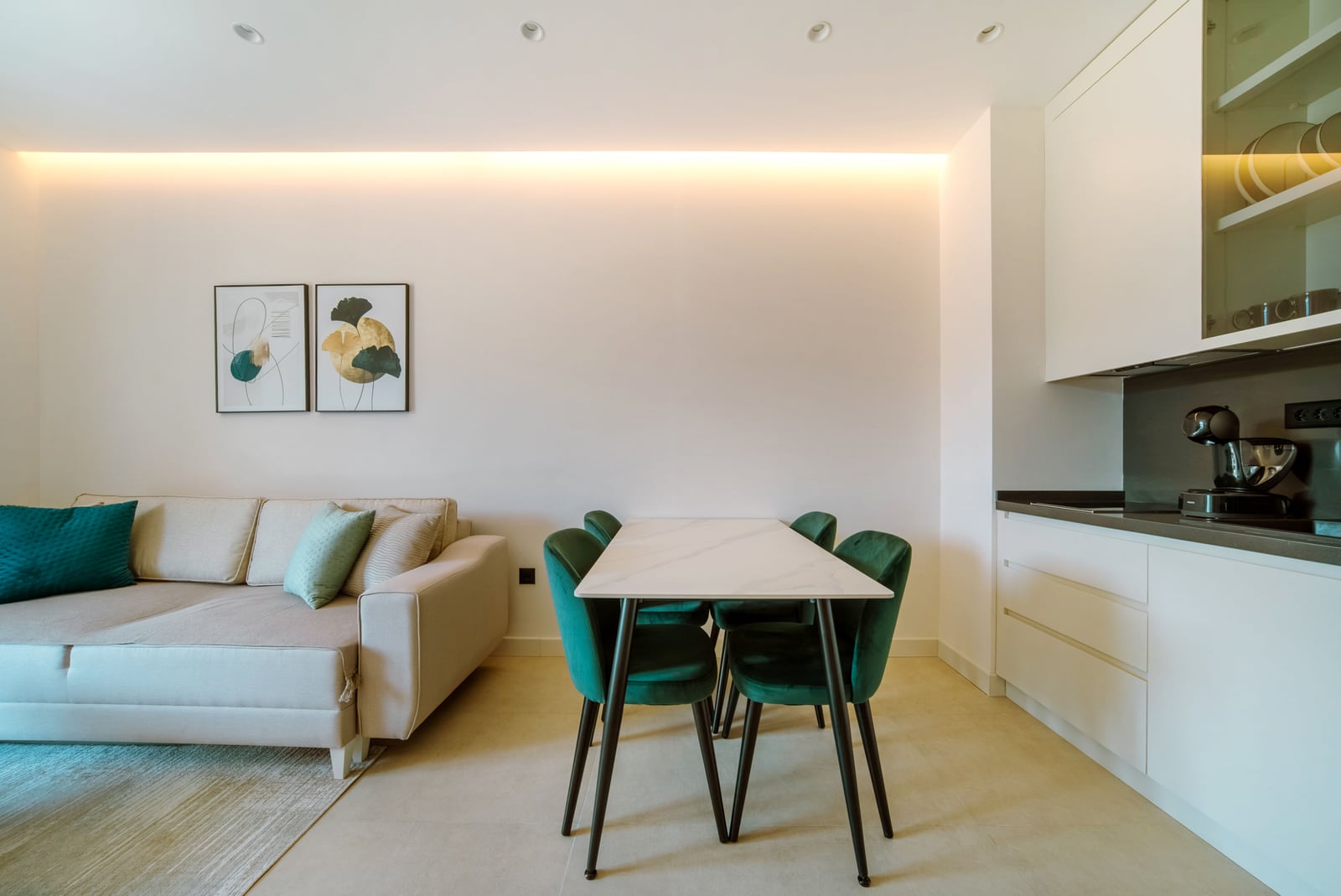 Modern living room with kitchen in an apartment in Bečići, Montenegro: beige sofa, dining table, and green chairs.