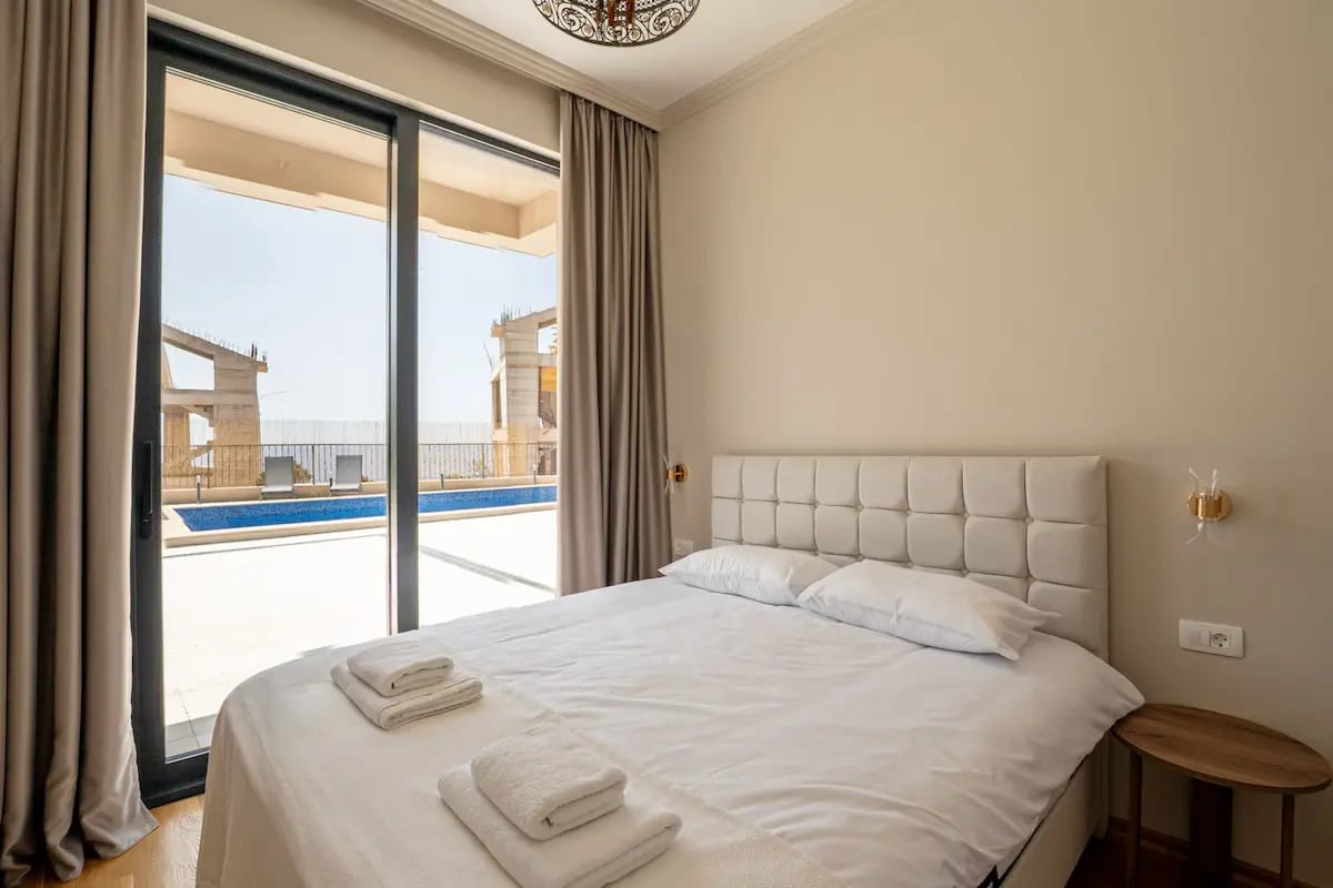 Bedroom with a double bed and pool access in a villa in Reževići, Montenegro. Modern interior with panoramic windows.
