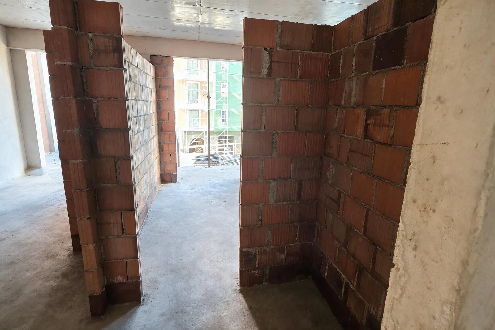Unfinished construction space with exposed red brick partition walls, bare concrete floor, and raw ceiling structure.