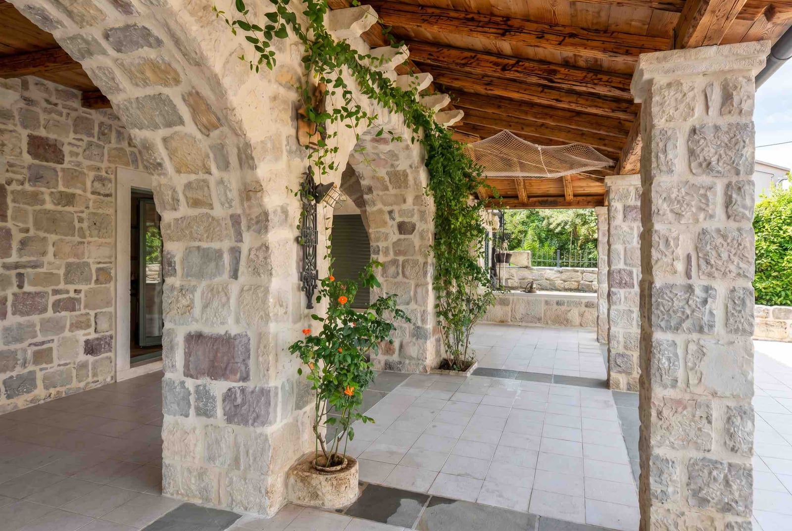 Covered stone terrace with arches in a house on the Luštica Peninsula, Montenegro: traditional finishes and garden view.