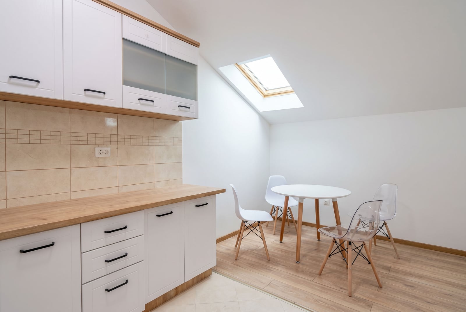 Modern kitchen in an attic apartment in Budva, Montenegro: white cabinetry, dining area, and skylight.