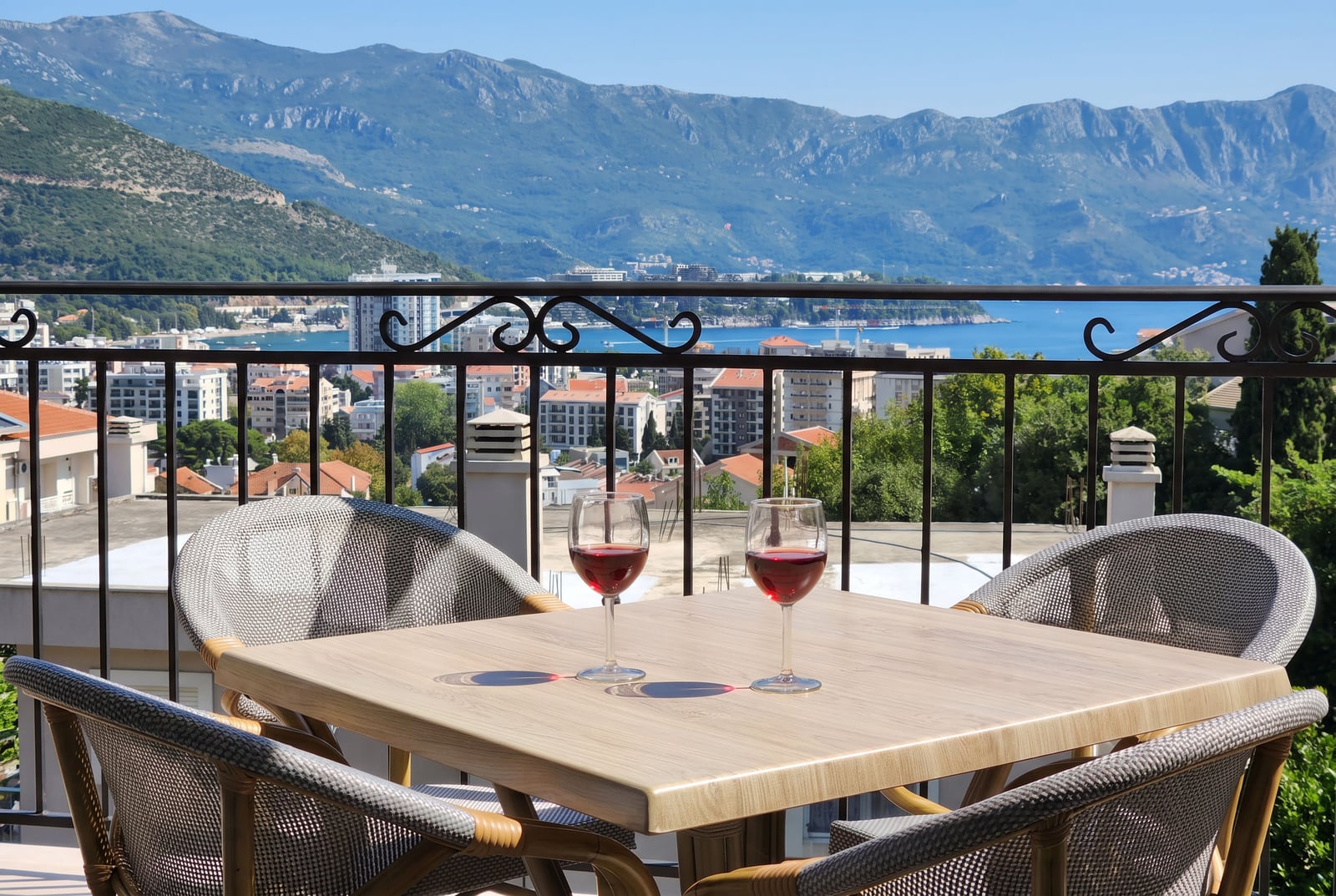 Balcony with wicker furniture and a view of the sea and mountains in an apartment, Budva, Montenegro. Two glasses of wine on the table.