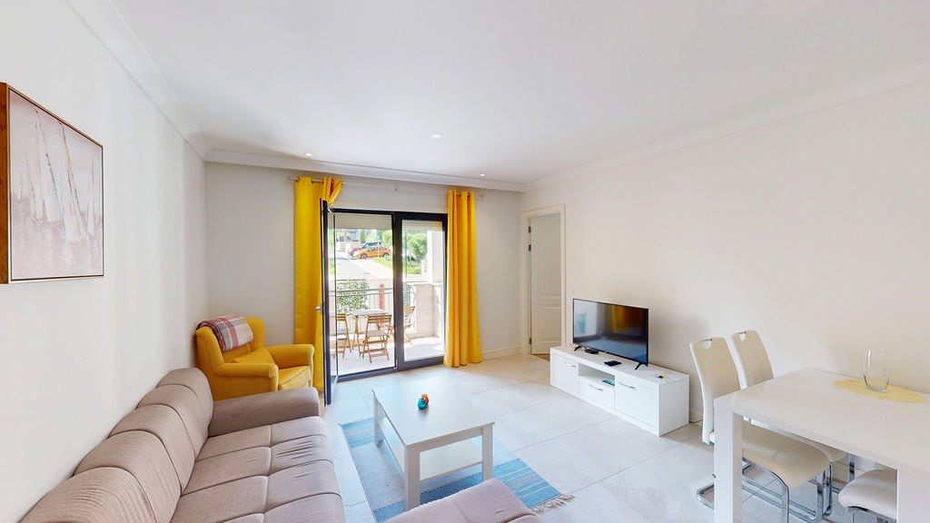 Bright living room in an apartment, Luštica, Montenegro: beige sofa, yellow armchair, dining area, and access to the terrace.