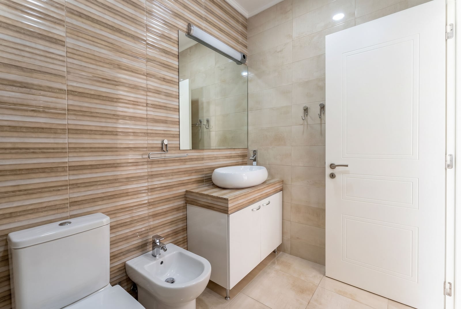 Modern bathroom in an apartment, Budva, Montenegro: white sanitary ware, bidet, vanity unit with sink, and beige-toned tiles.