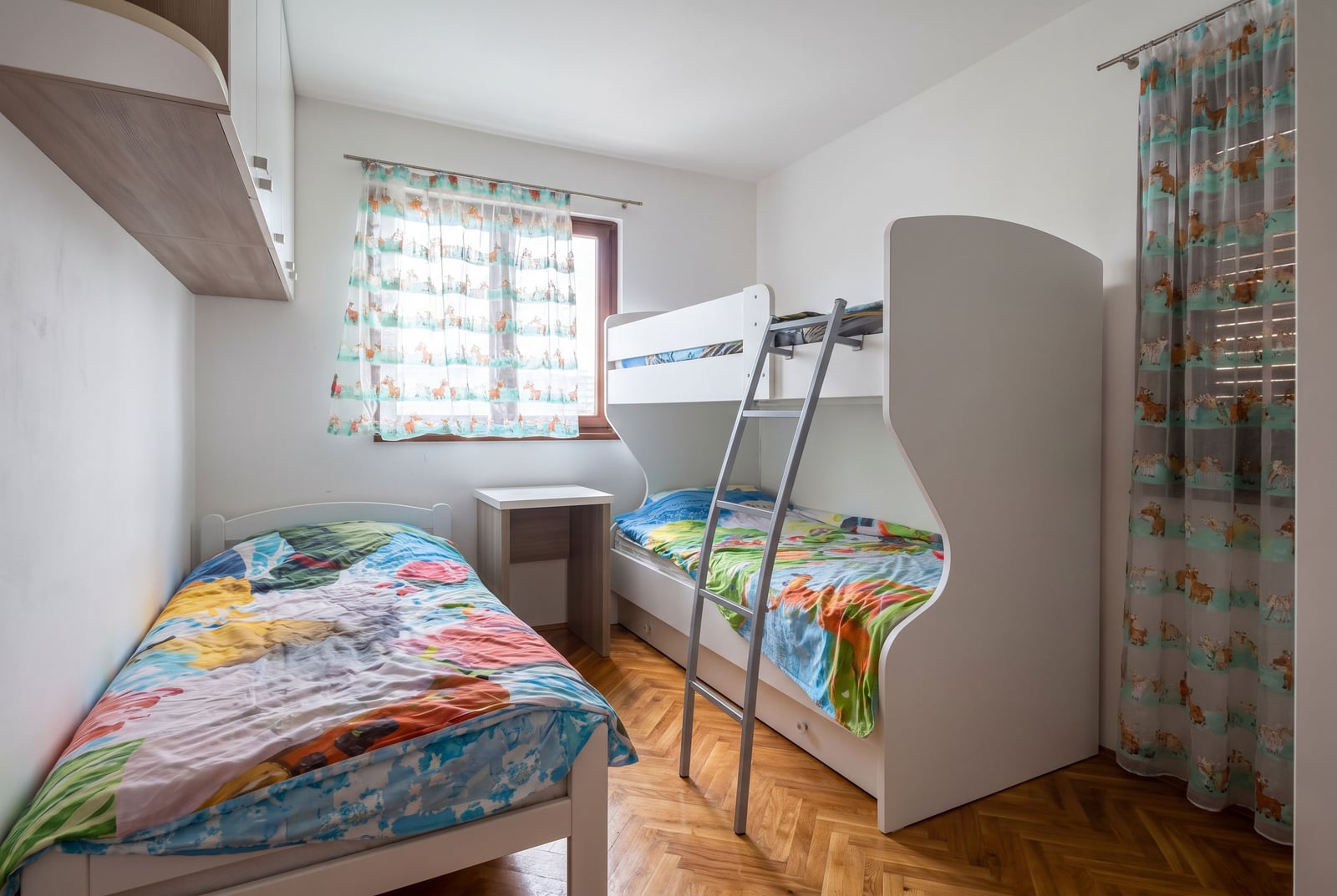 Children's bedroom featuring a single bed and a bunk bed with colorful bedding on parquet flooring.