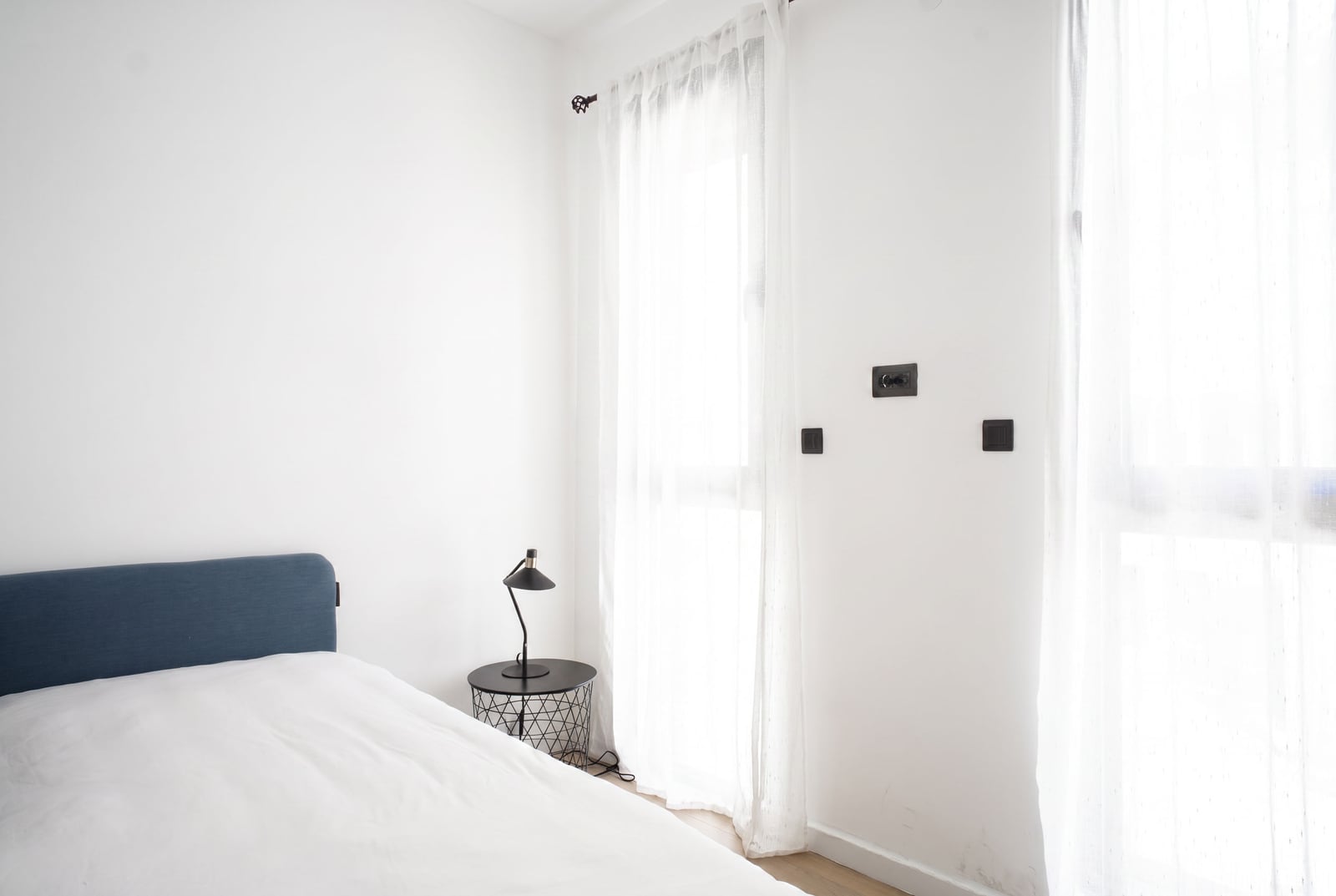 Bright bedroom with white walls, a bed with a blue headboard, and a nightstand in an apartment in Tivat, Montenegro