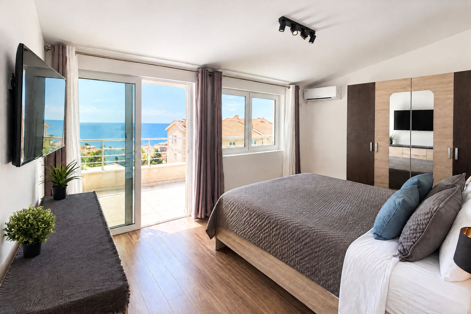 Modern bedroom with a double bed, wardrobe, and balcony door overlooking the sea.